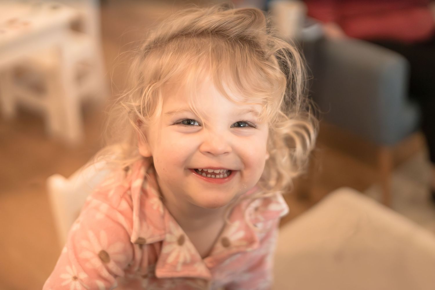 Young child smiling brightly in warm indoor lighting.