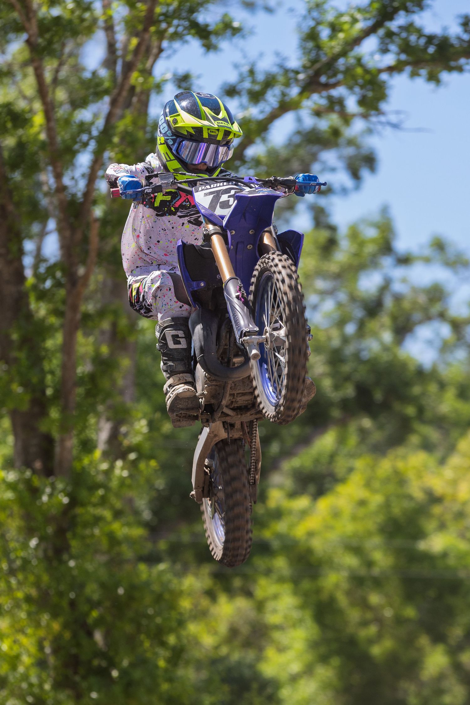 Dirt bike rider performing high jump with trees in background.