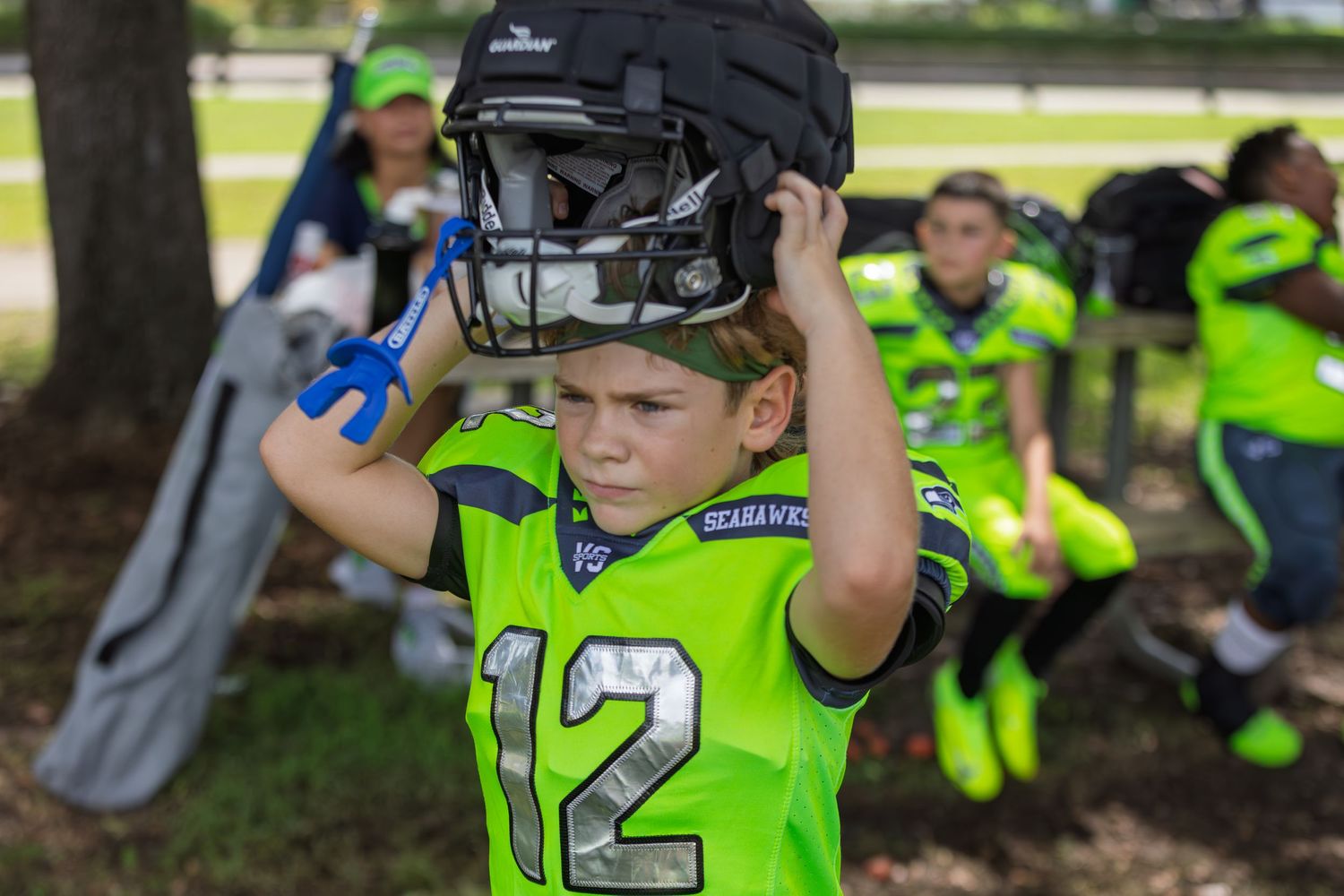 Youth sports players in neon yellow jerseys watching from sidelines.