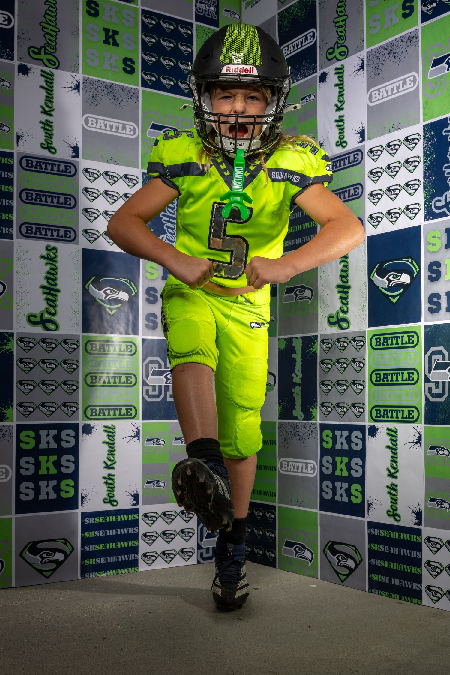 Youth athlete in bright yellow uniform poses against branded backdrop.