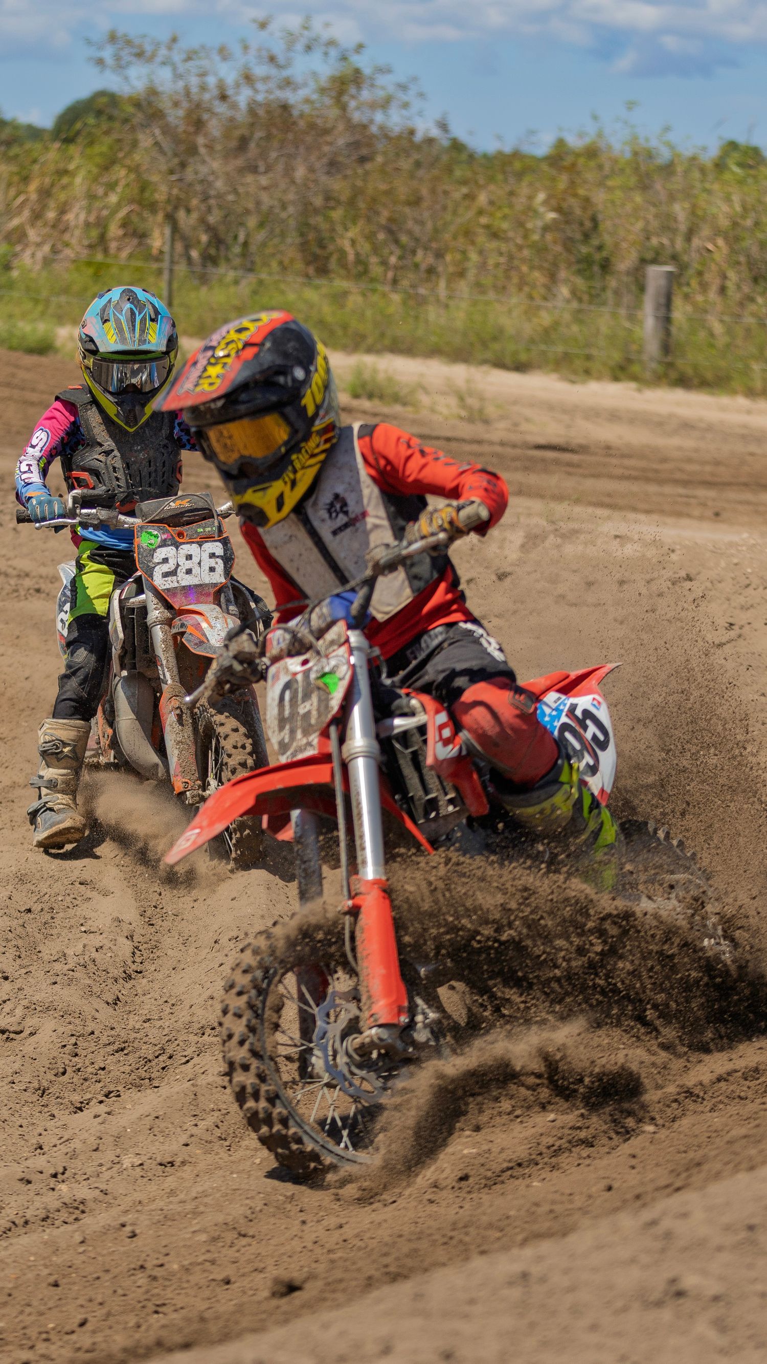 Motocross riders kicking up dirt while racing around a dirt track corner.