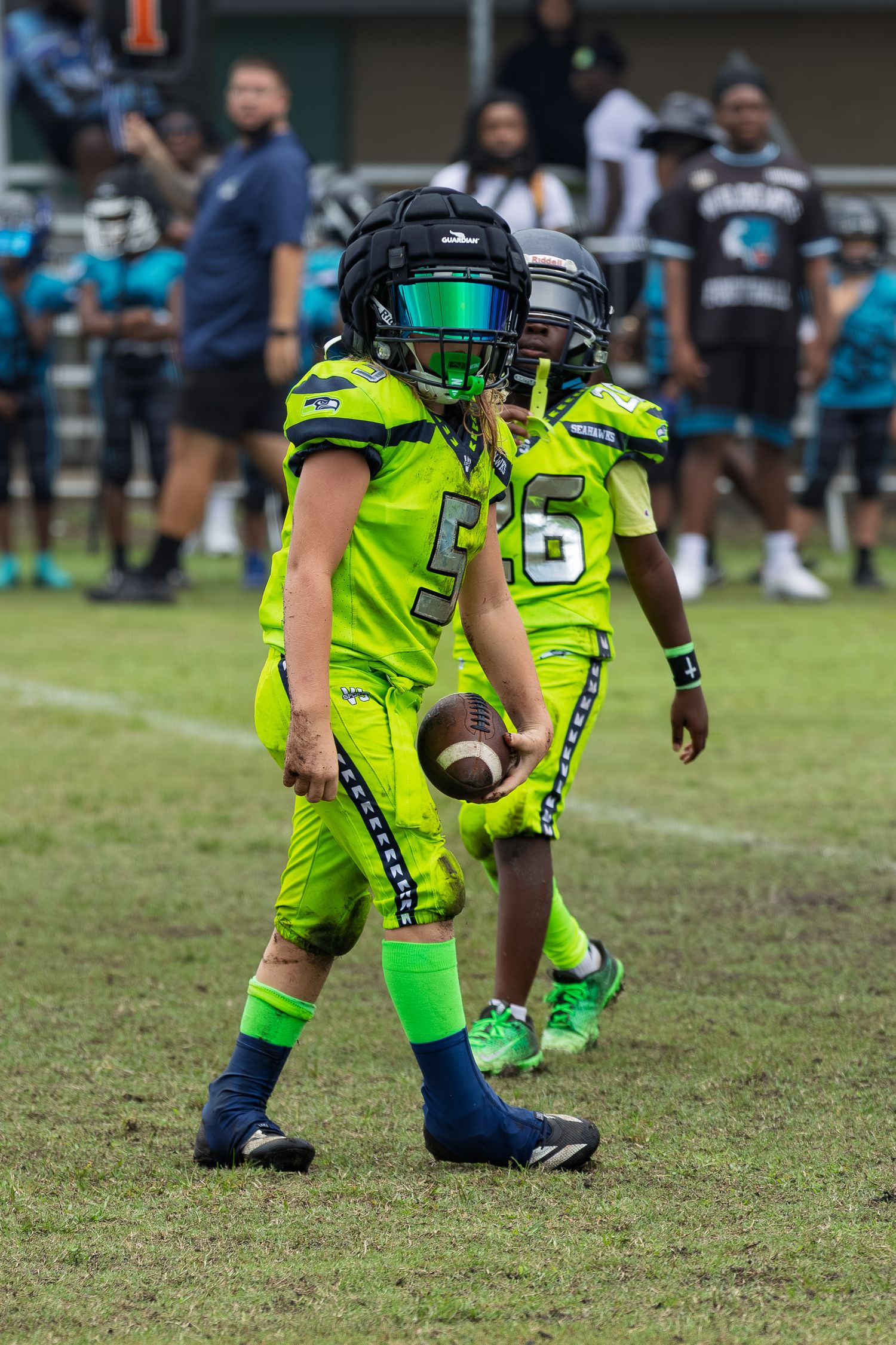 Youth football players in bright neon green uniforms running on a grass field during a game.