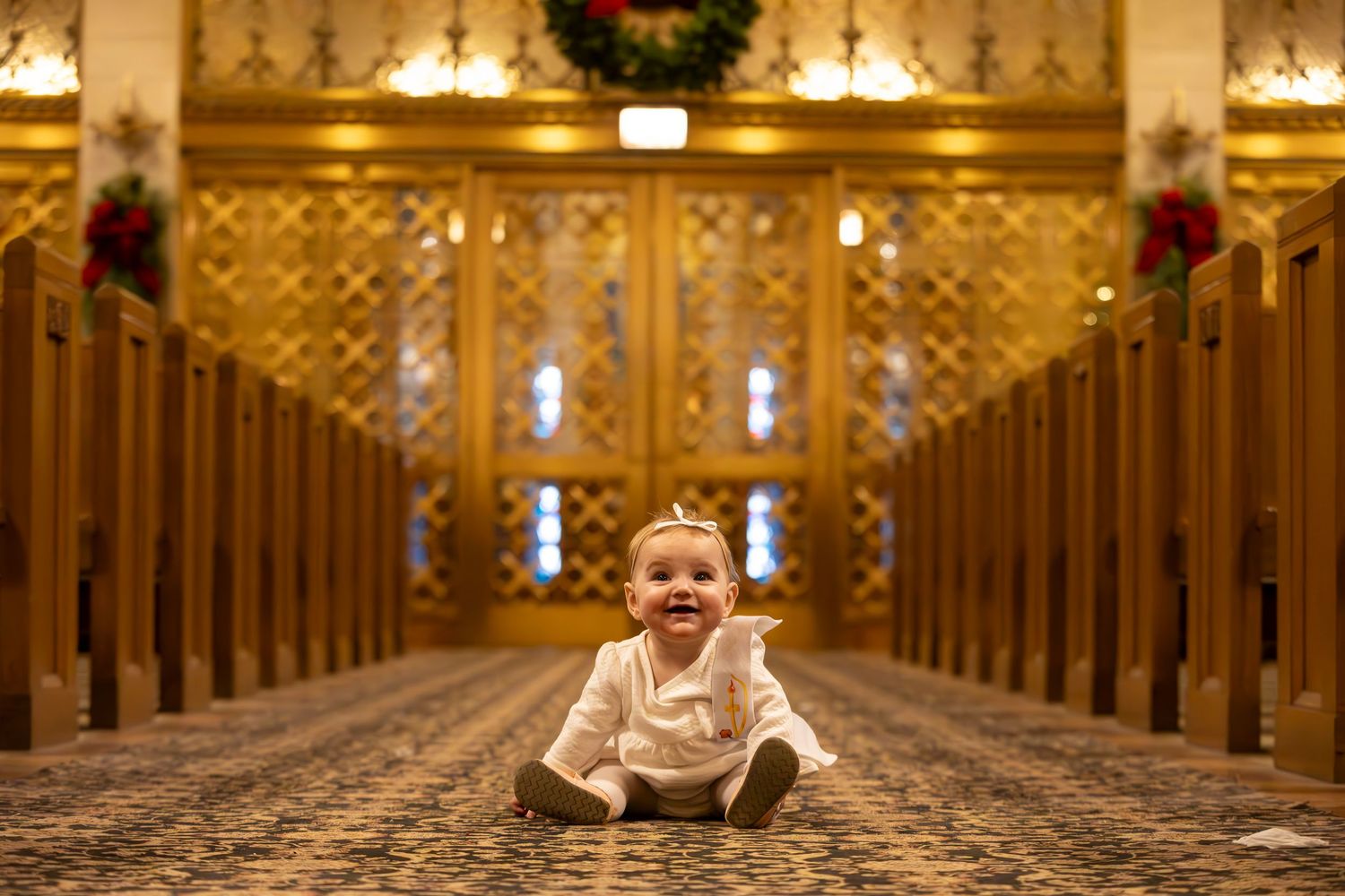 Interior view of an ornate church with wooden pews and golden decorative elements stretching into the distance. with baby at baptism