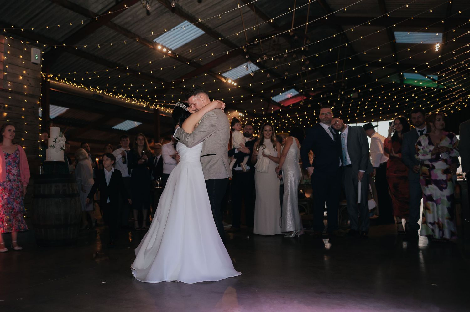 Newlyweds share their first dance under twinkling fairy lights at an indoor wedding reception venue.