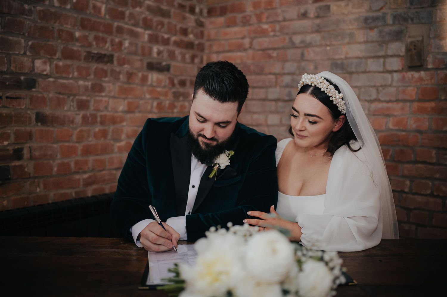 A couple signing marriage documents at their wedding ceremony with white floral decorations.