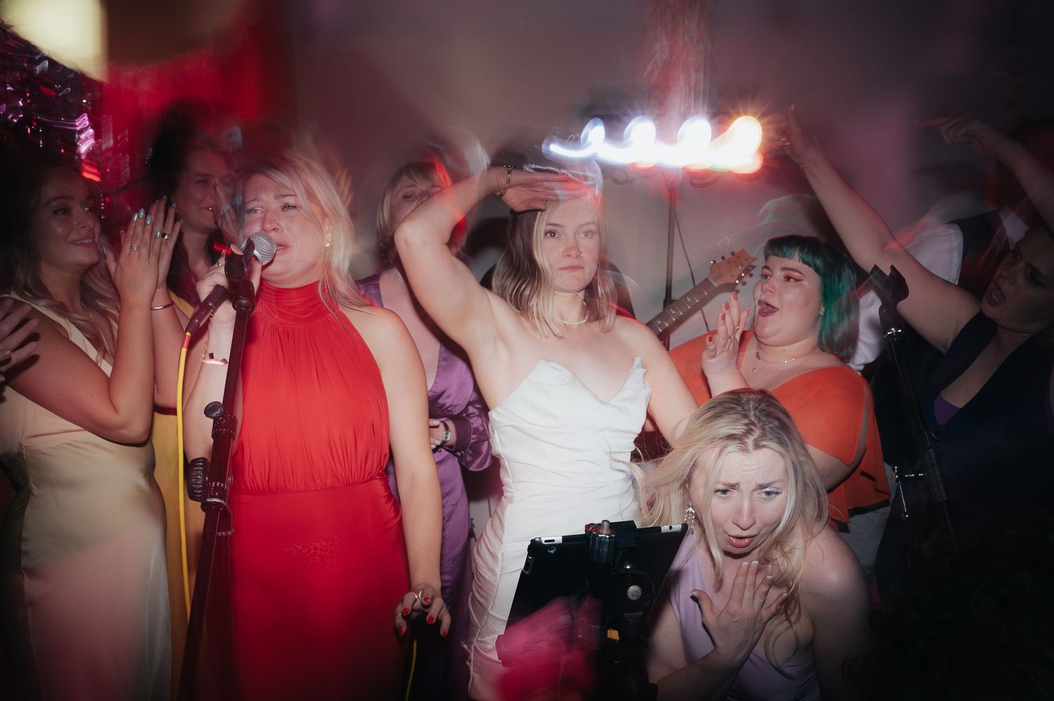 Wedding reception party goers dancing energetically on a dark dance floor with colorful lighting effects.