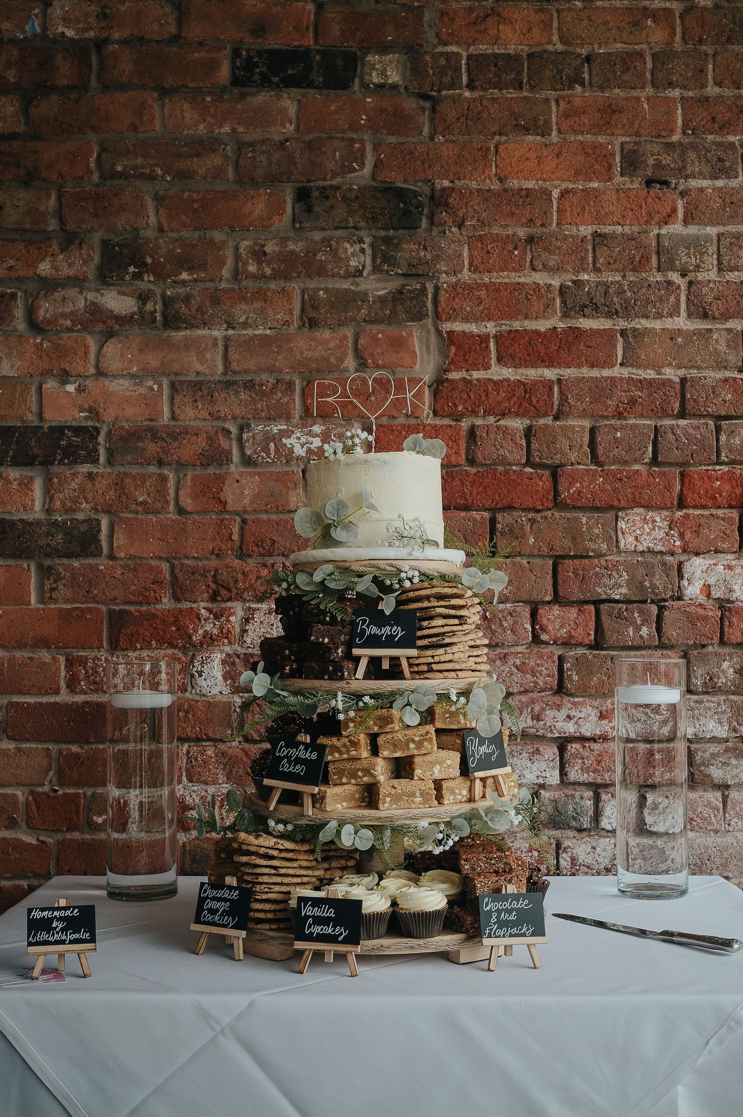 Multi-tiered wedding dessert display with pancakes and cake against exposed brick wall.