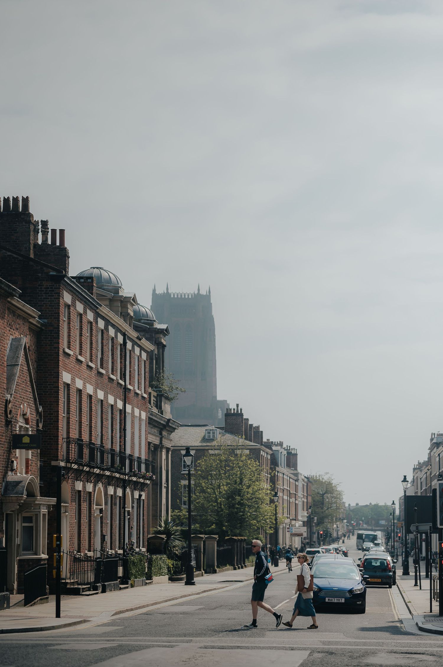 Historic English street scene with brick buildings and church spire visible in the misty background.