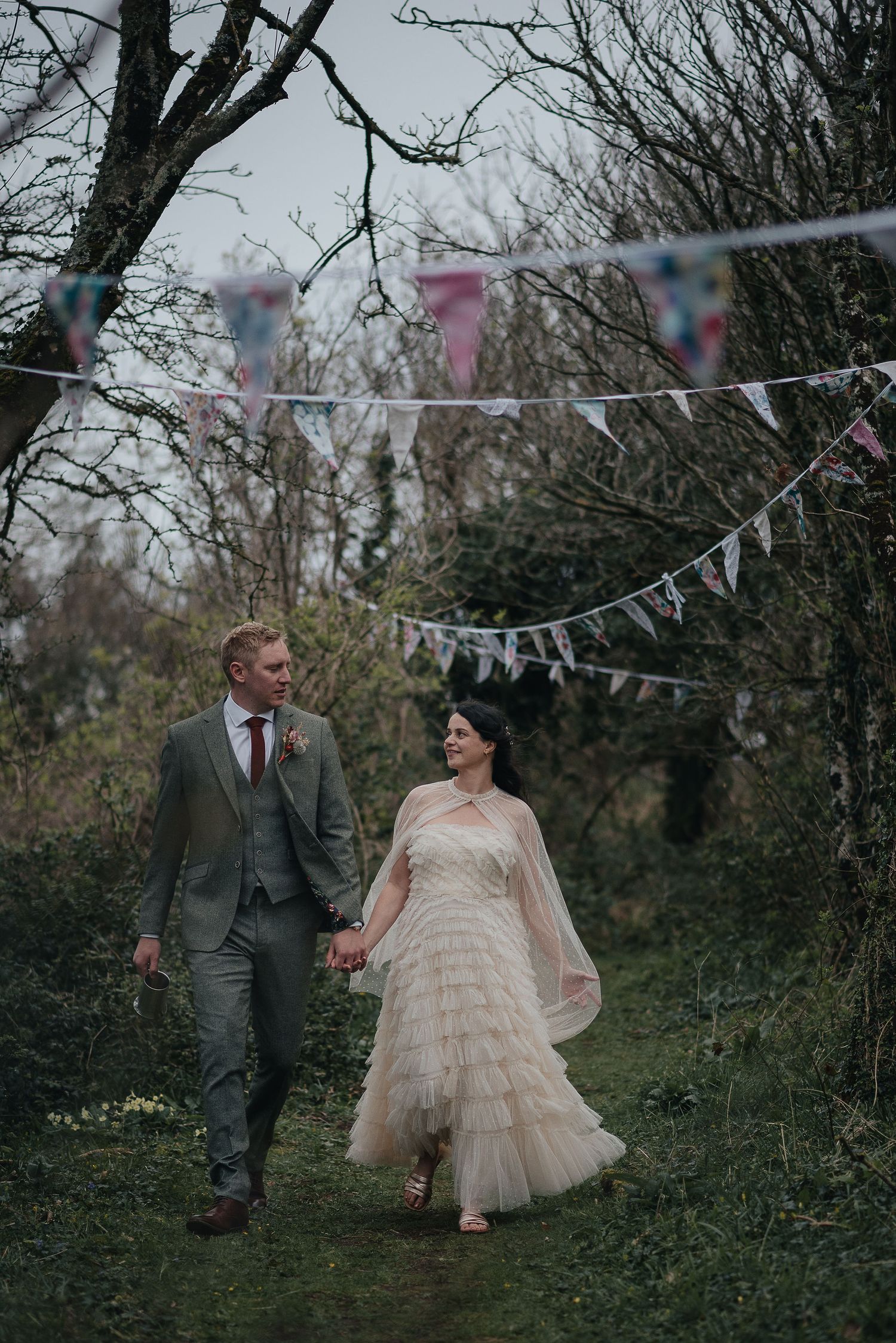 A couple walking under bunting decorations in a woodland wedding setting.