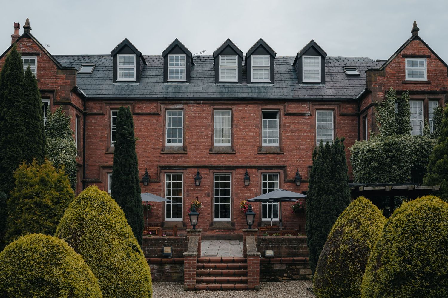 Elegant red brick building with dormer windows and manicured topiary bushes in front.