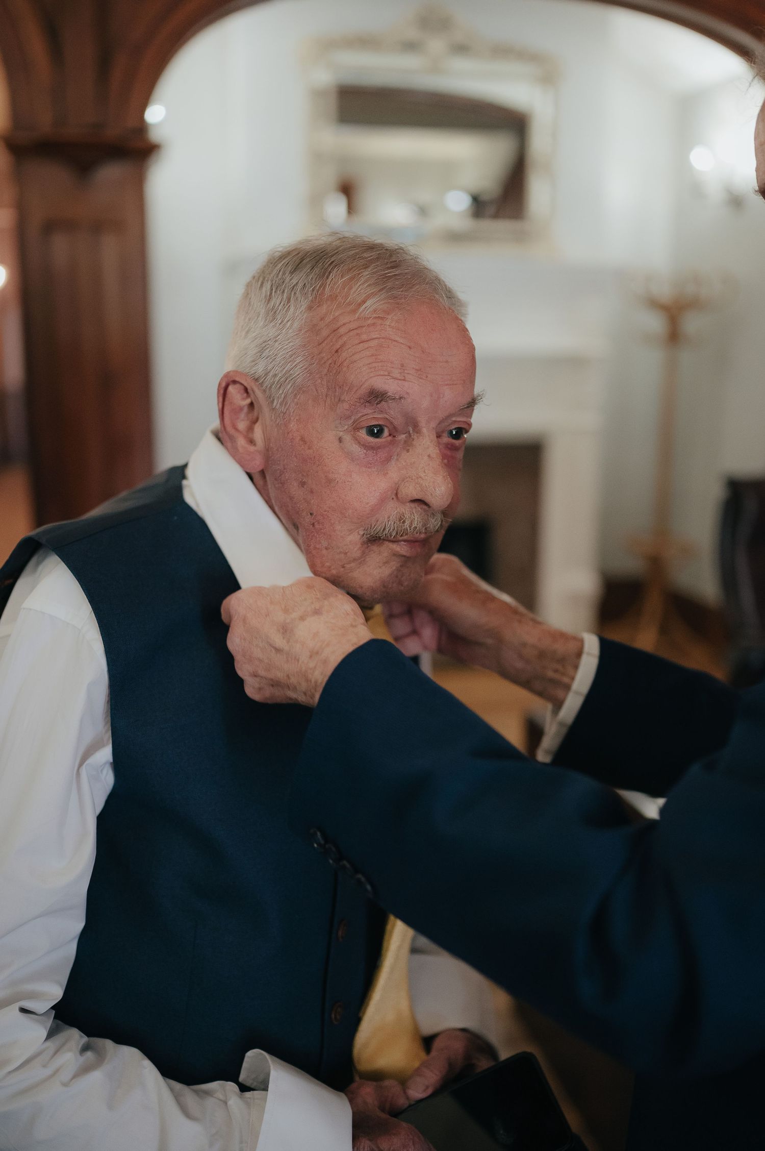 Senior gentleman adjusts his navy vest while getting dressed for formal occasion.
