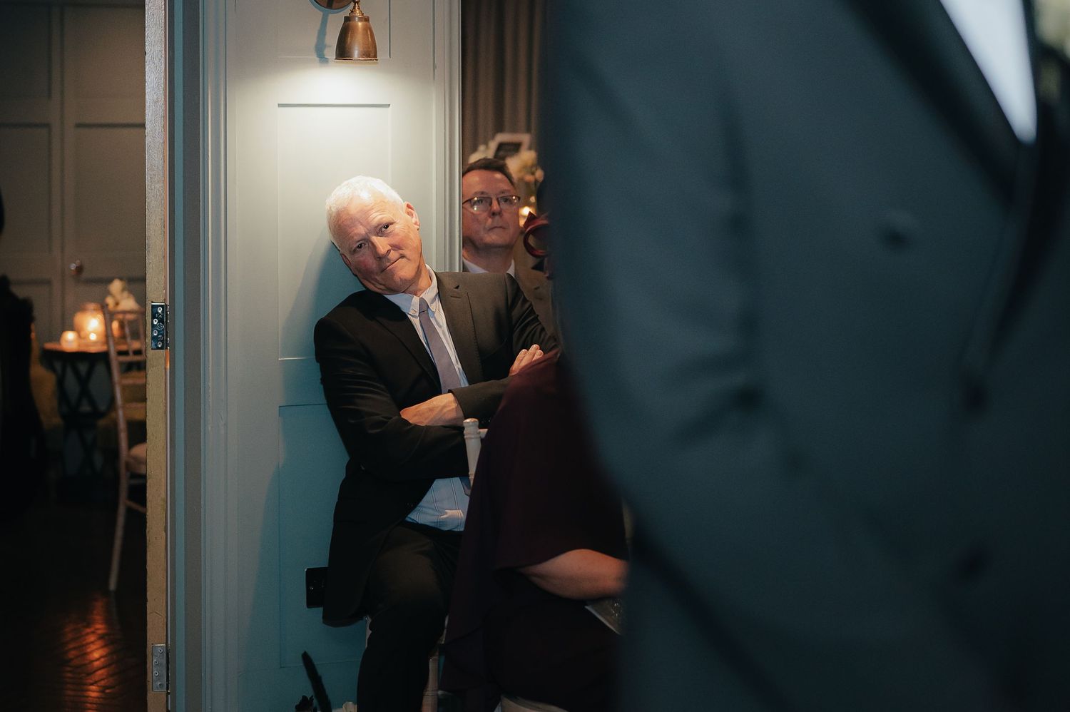 Two people share a loving moment in a dimly lit hallway under a pendant light.