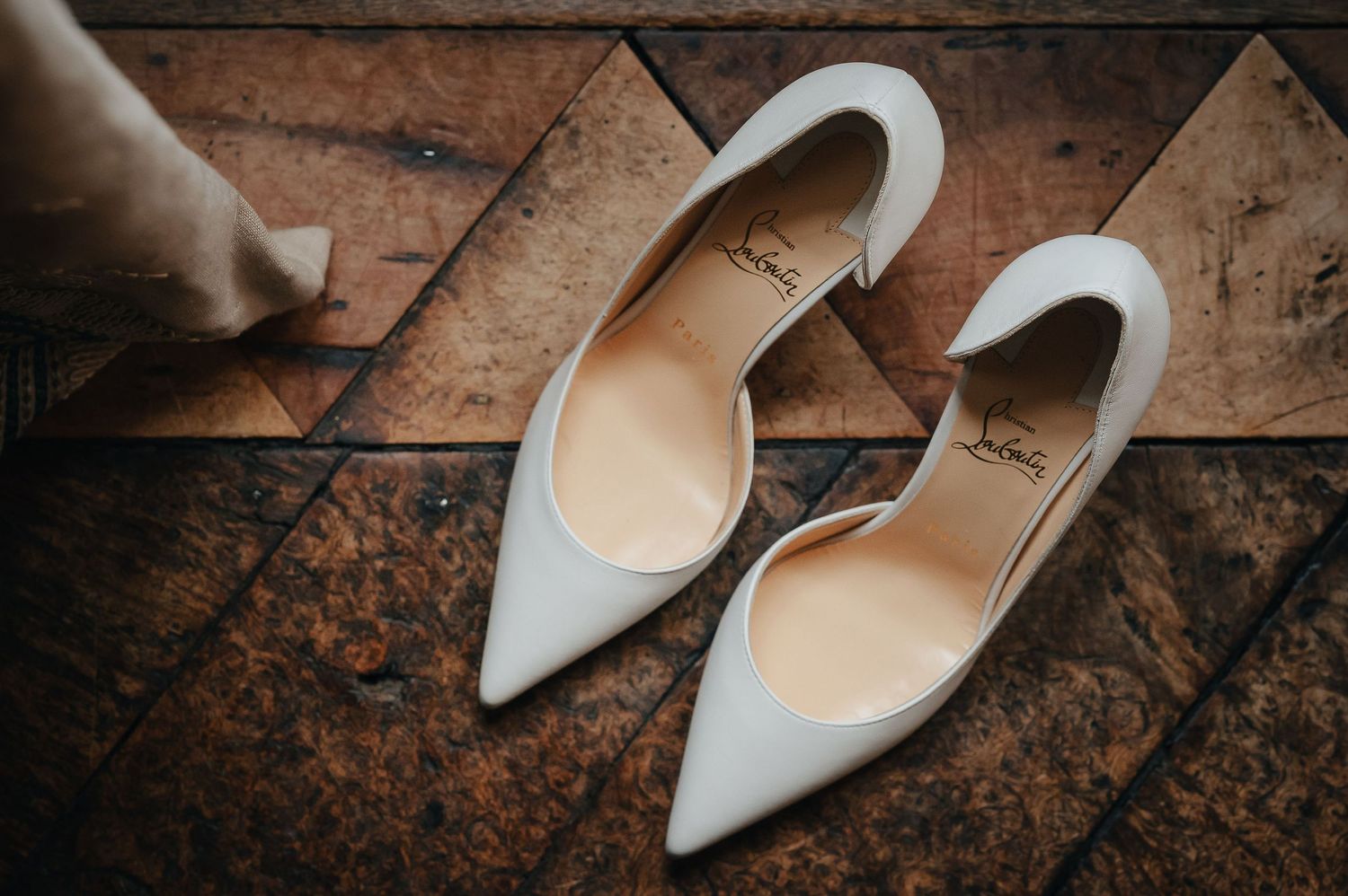Elegant white pointed-toe bridal shoes on a rustic wooden surface.