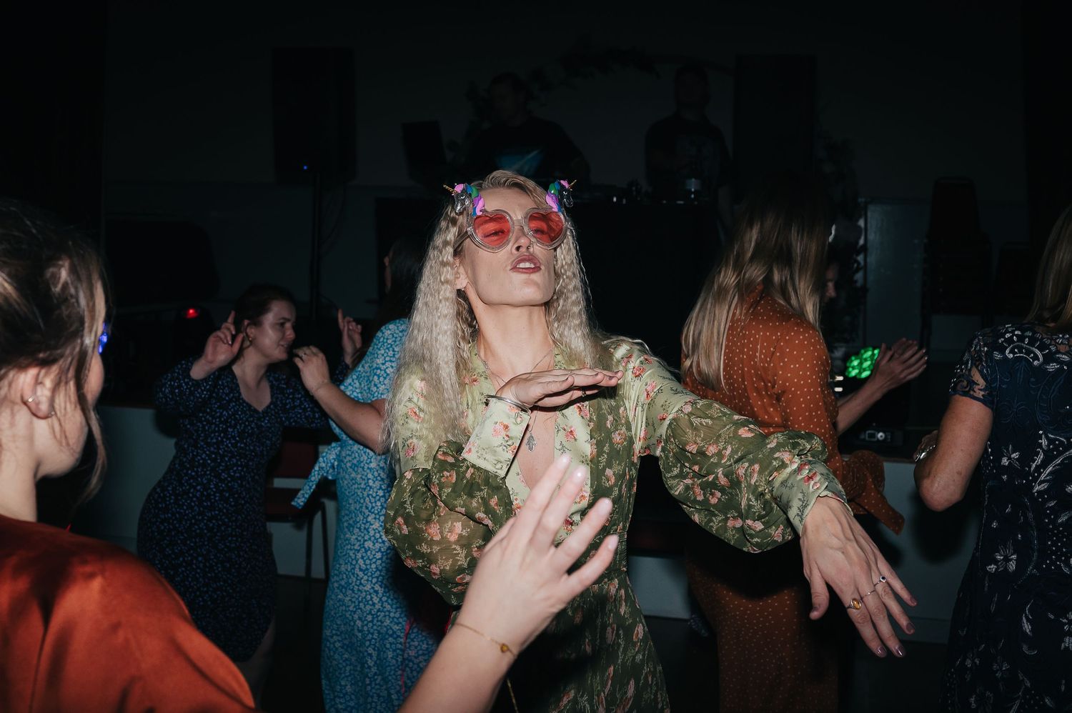 A partygoer dances with enthusiasm wearing pink sunglasses and a metallic dress.