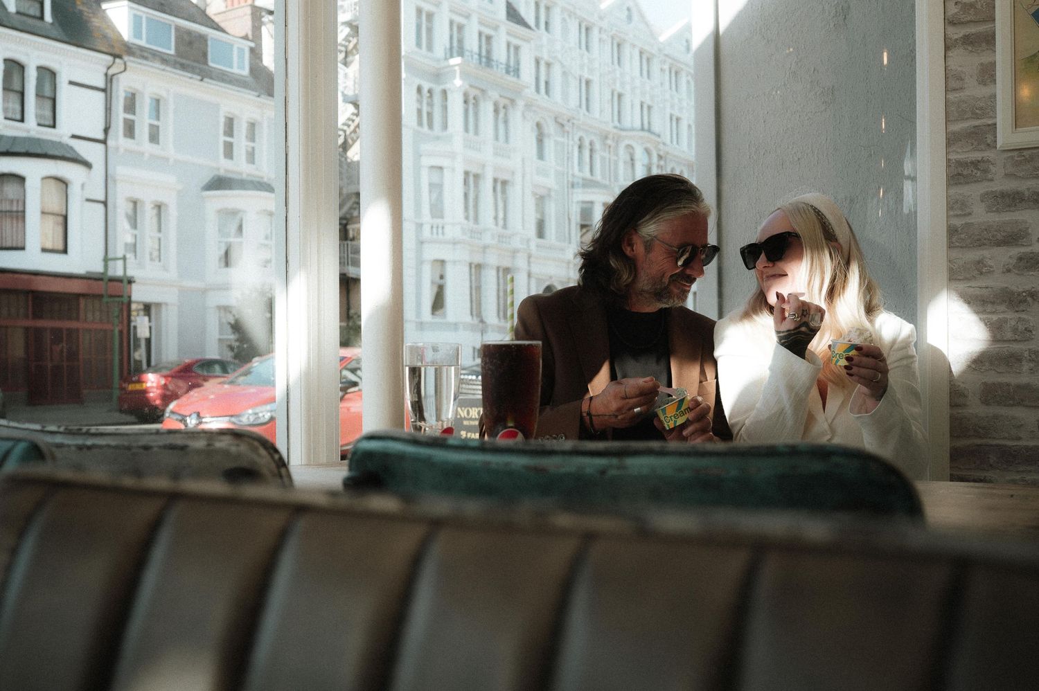 Two people sitting together in a cozy booth by a window in a cafe setting.