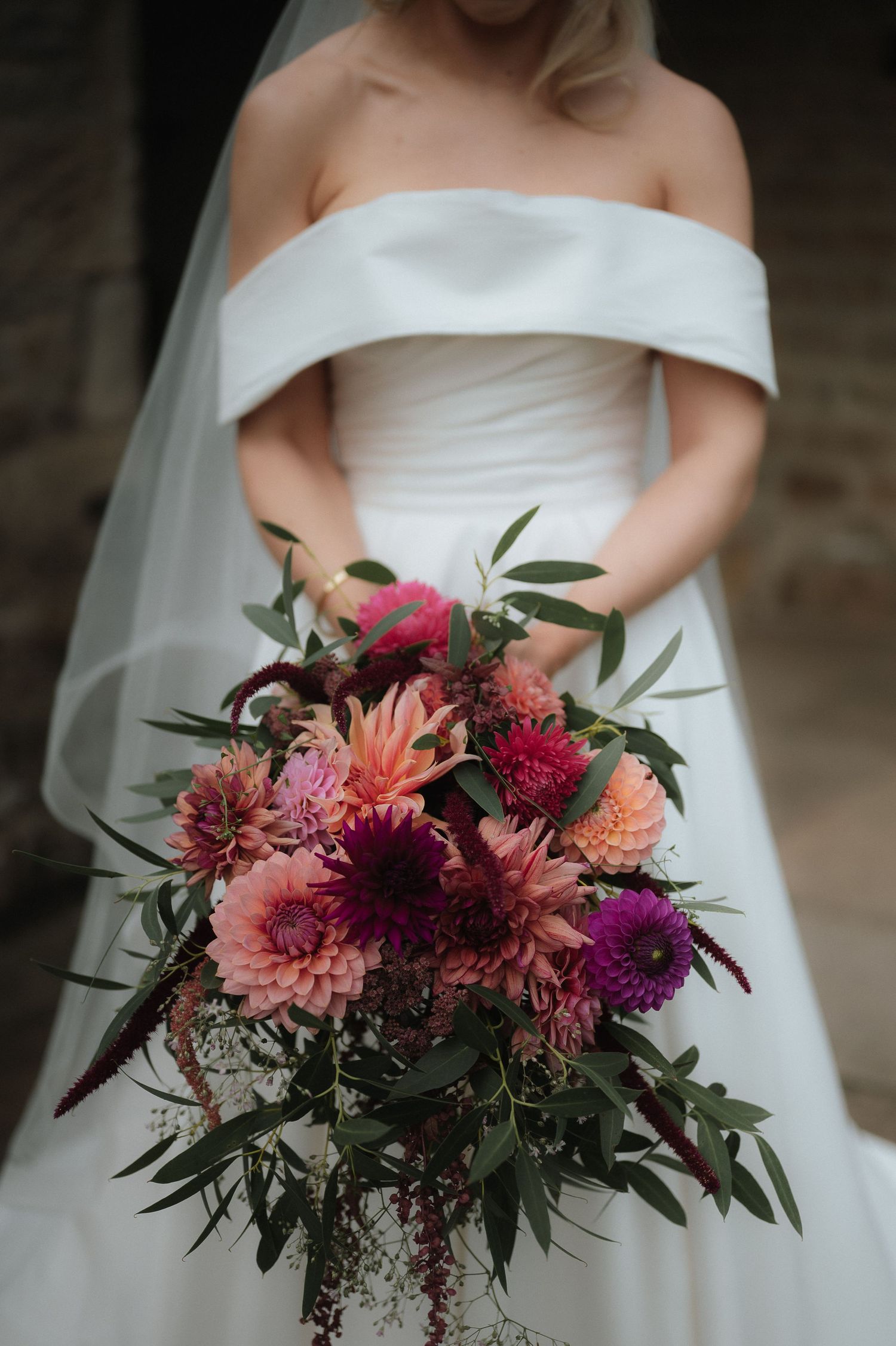 Elegant bridal bouquet featuring coral dahlias, deep burgundy blooms and fresh greenery against a white wedding dress.