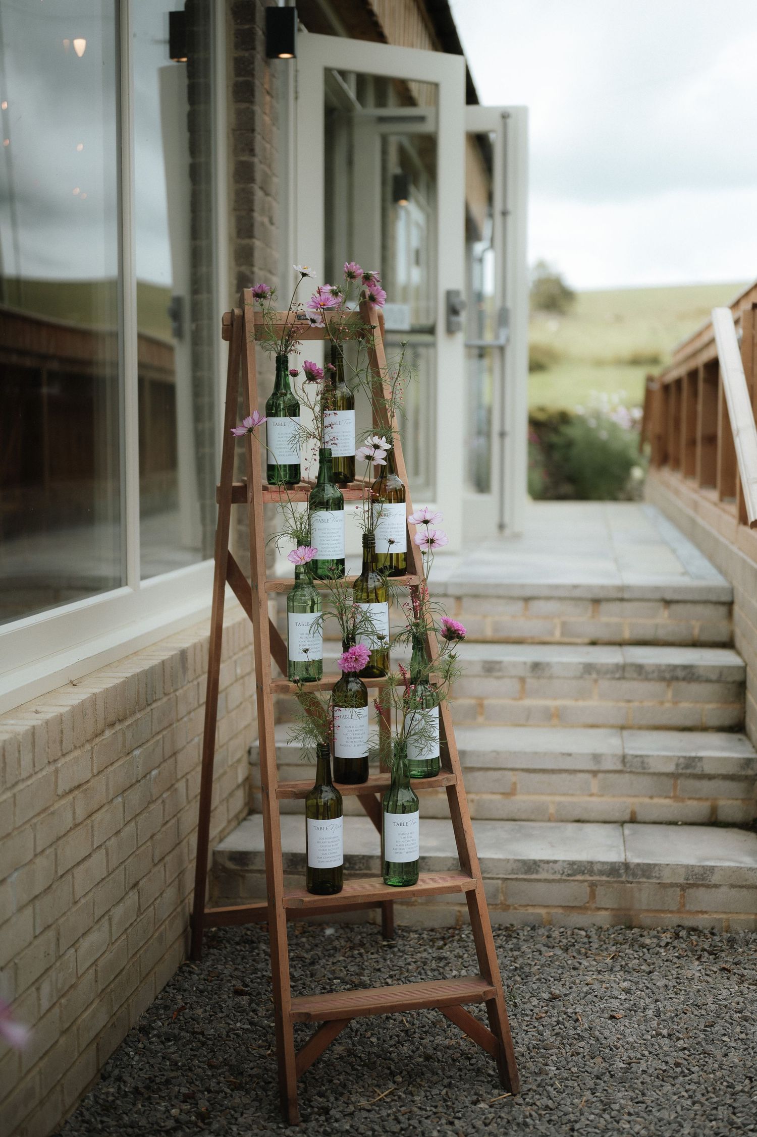 Rustic wooden ladder display with glass jars and pink flowers for wedding decor.