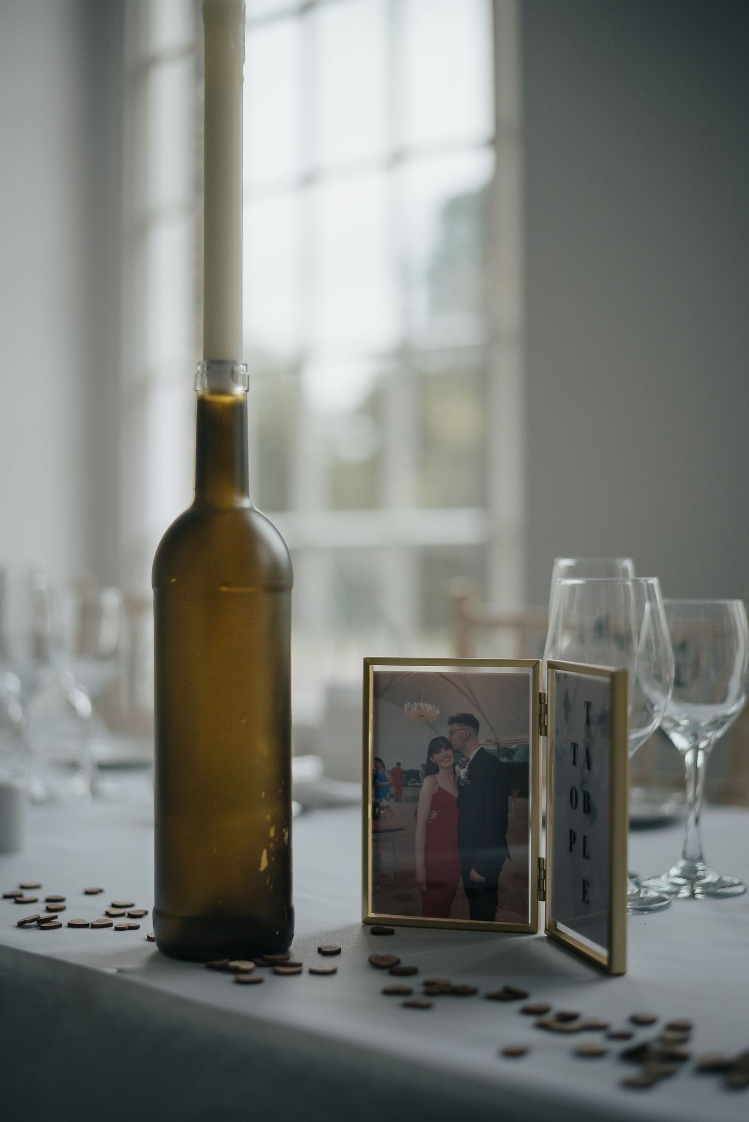 Wine bottle and picture frame displayed on table with scattered coins and wine glasses.