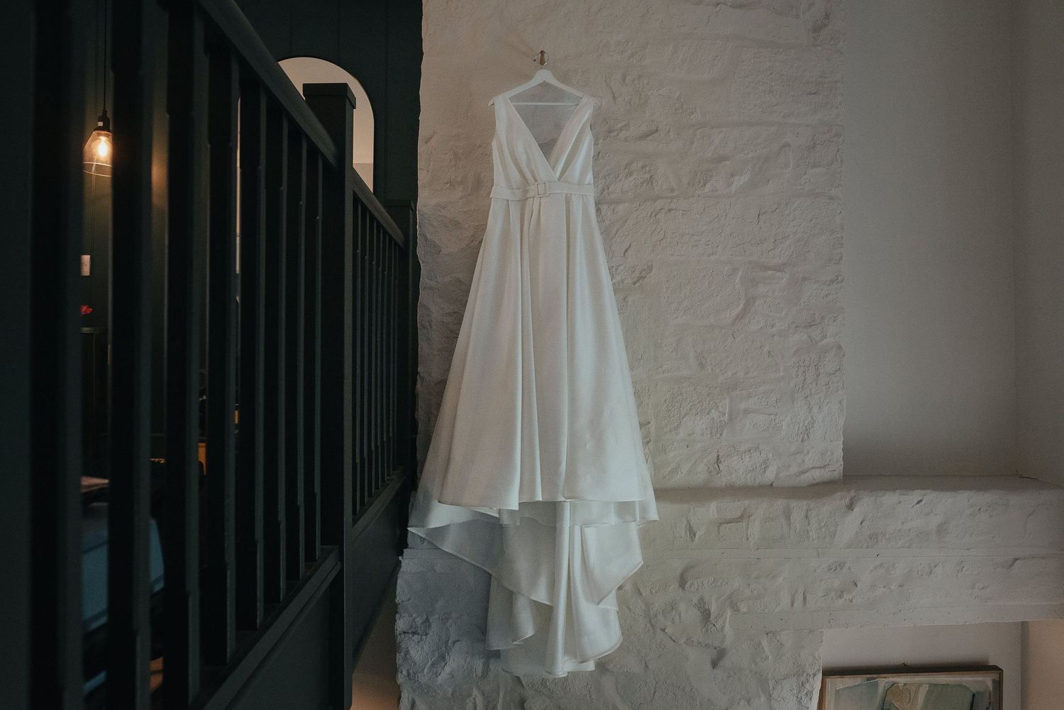 White wedding dress hanging against white wall with dramatic lighting.