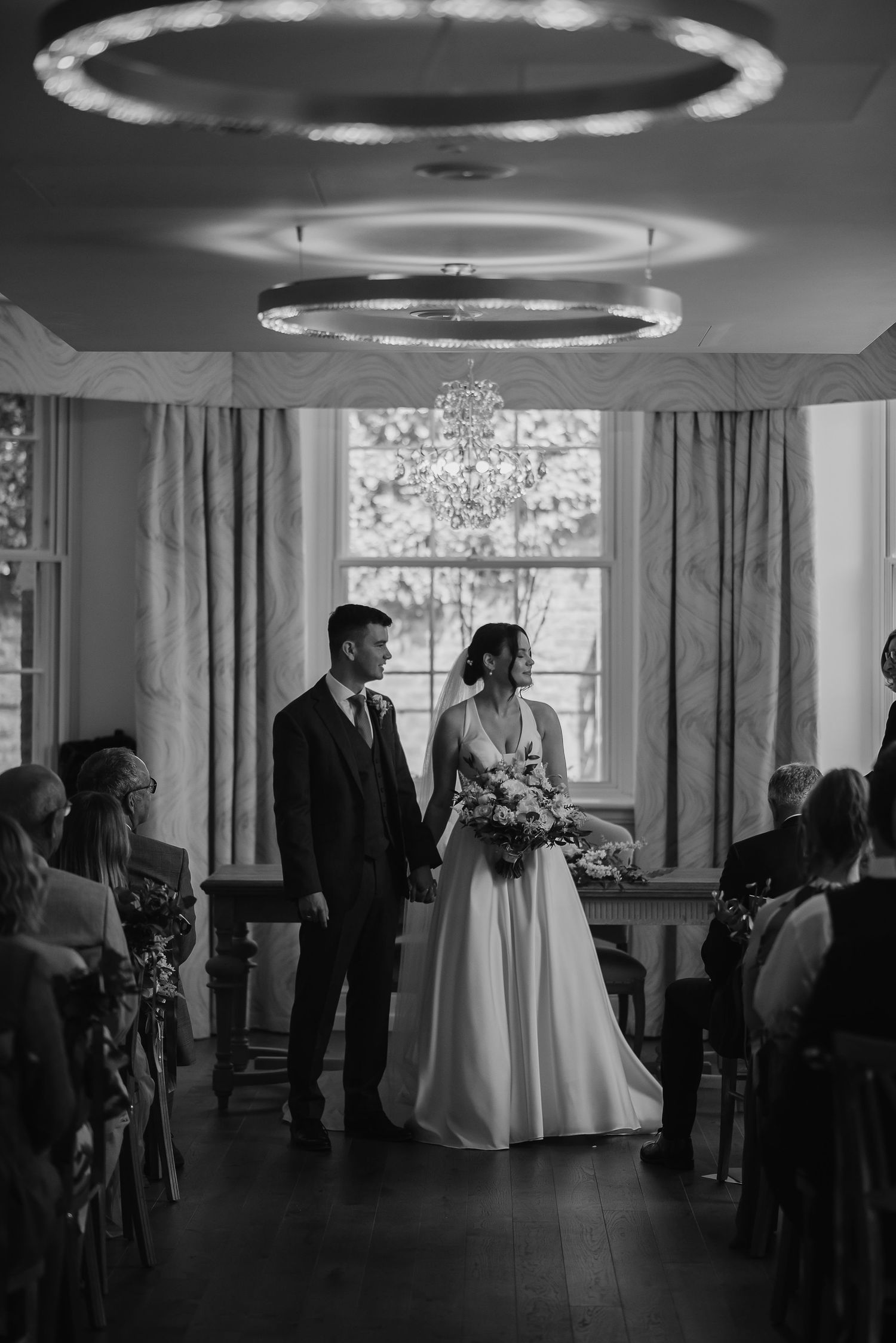 Black and white ceremony photo under distinctive circular ceiling lights in elegant venue.