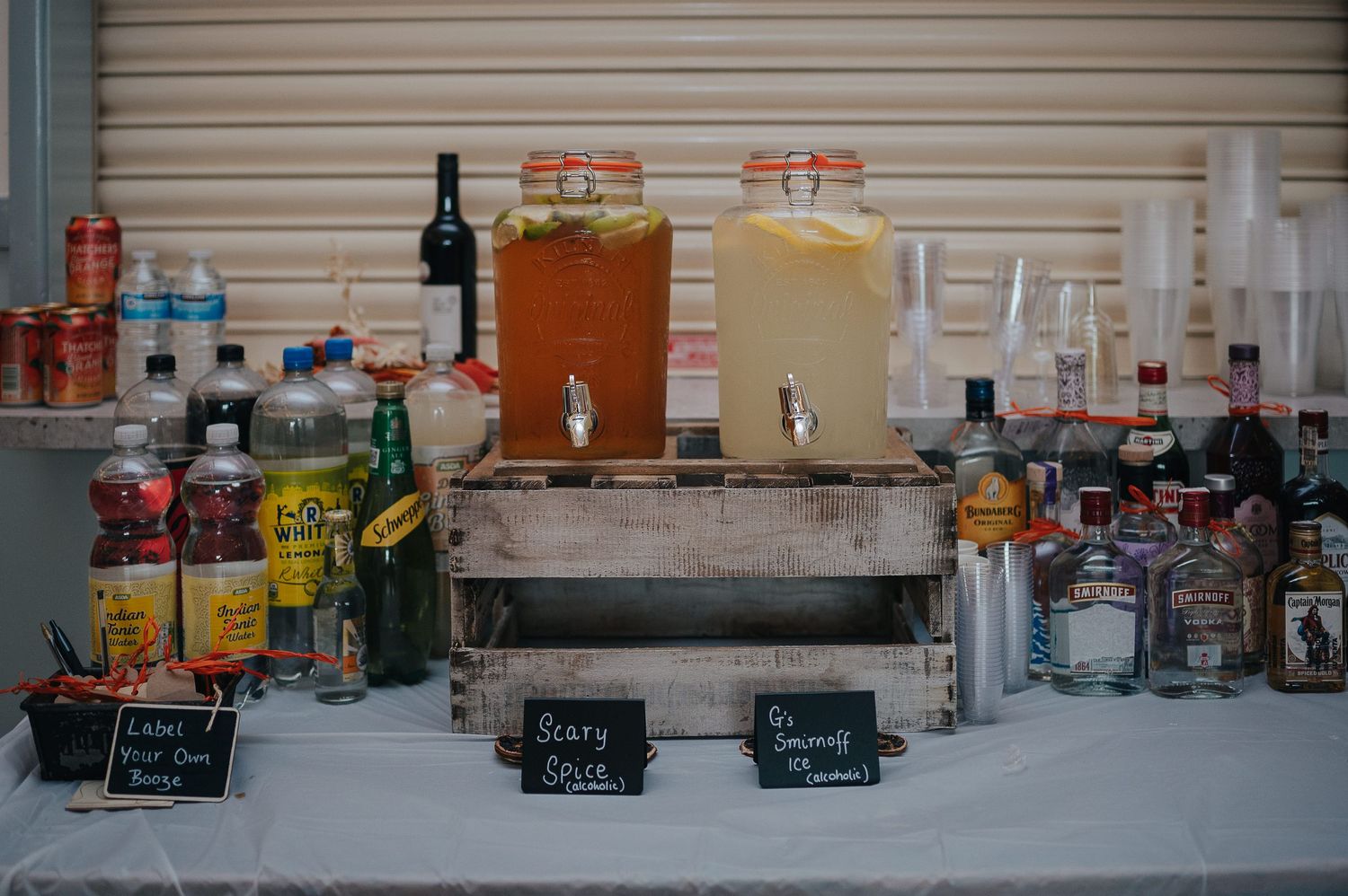 Wedding bar setup with beverage dispensers and various liquor bottles on a rustic wooden display.