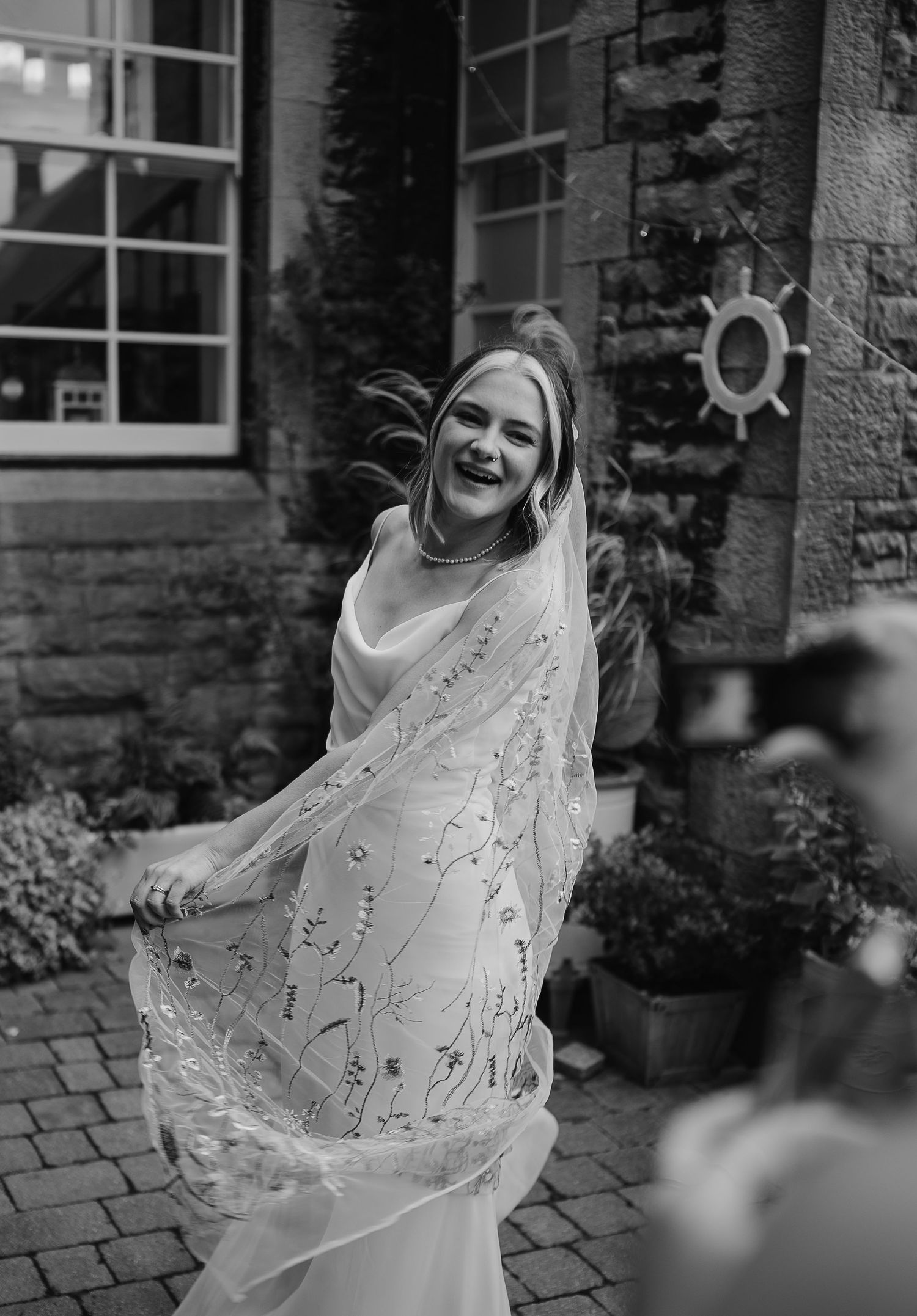 A joyful moment captured outside a stone building with a flowing wedding veil.
