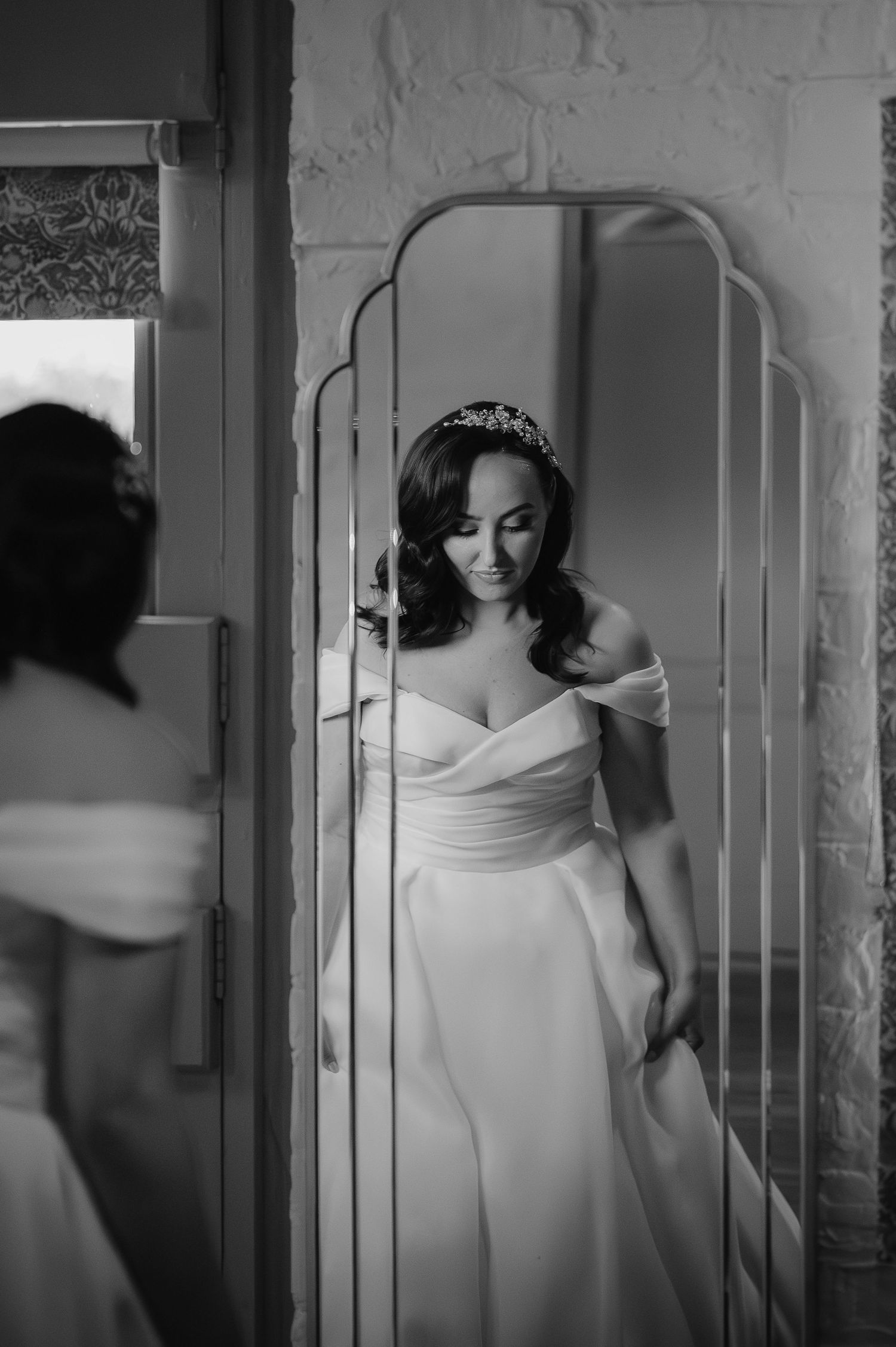 Black and white portrait of a bride in an off-shoulder dress looking in an art deco mirror.