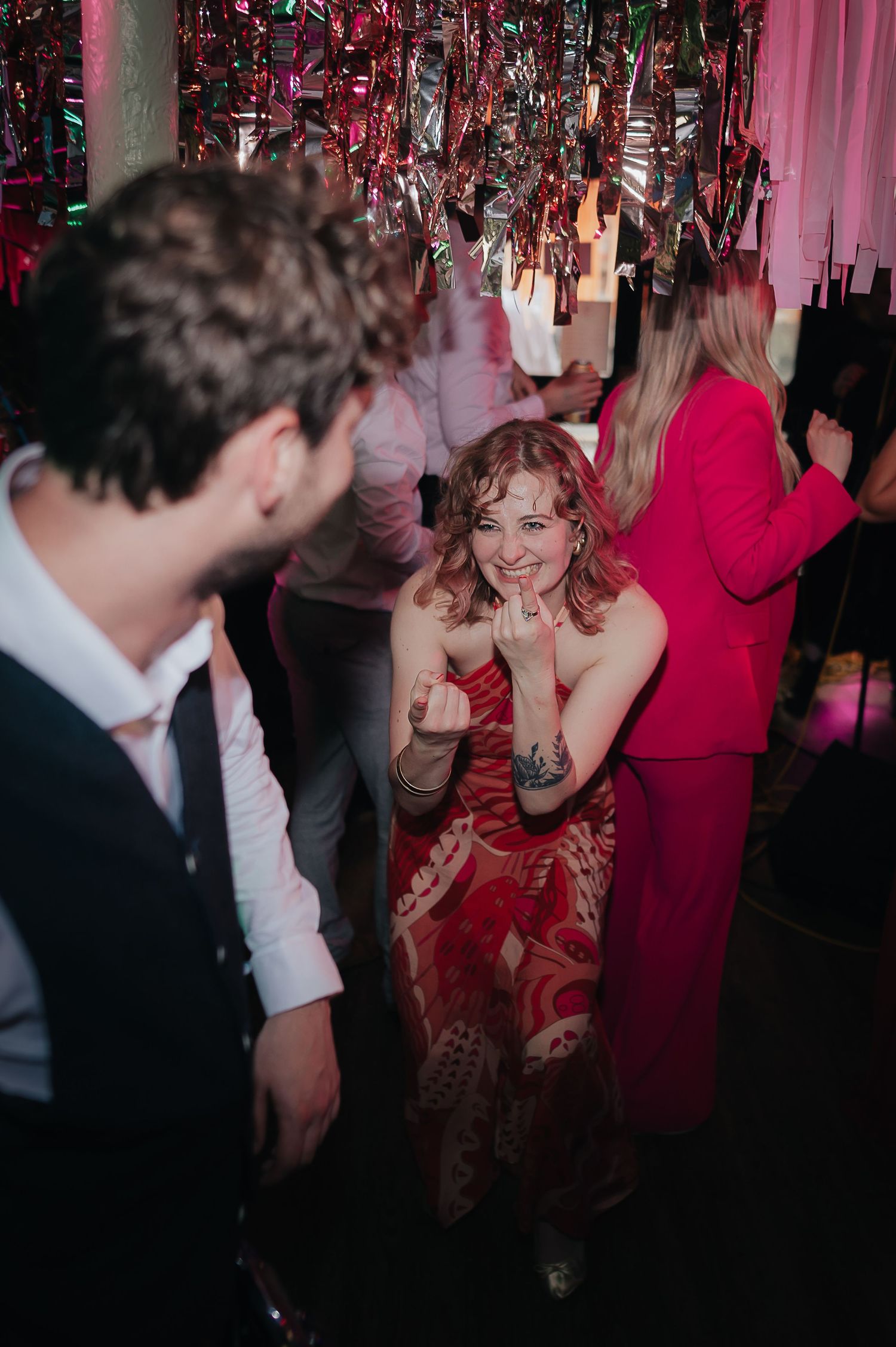 A festive celebration with pink decor where partygoers dance and smile beneath hanging decorations.