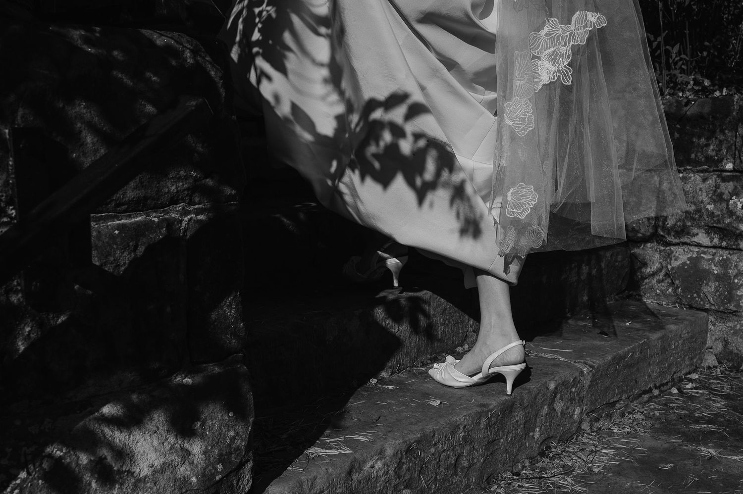 Black and white photo showing an elegant white bridal shoe against a dark stone background.