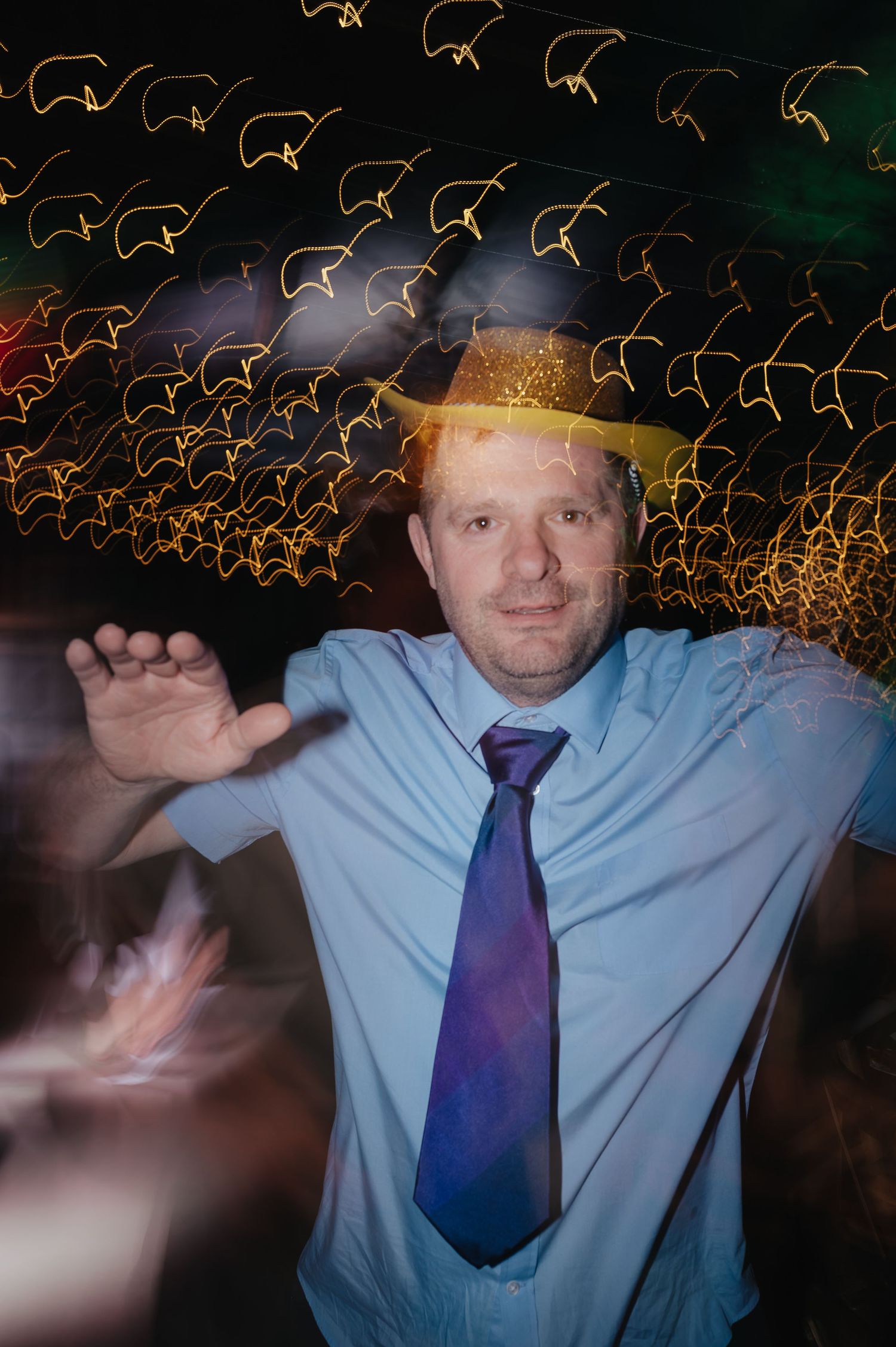 Wedding guest in blue tie dancing beneath decorative ceiling lights.