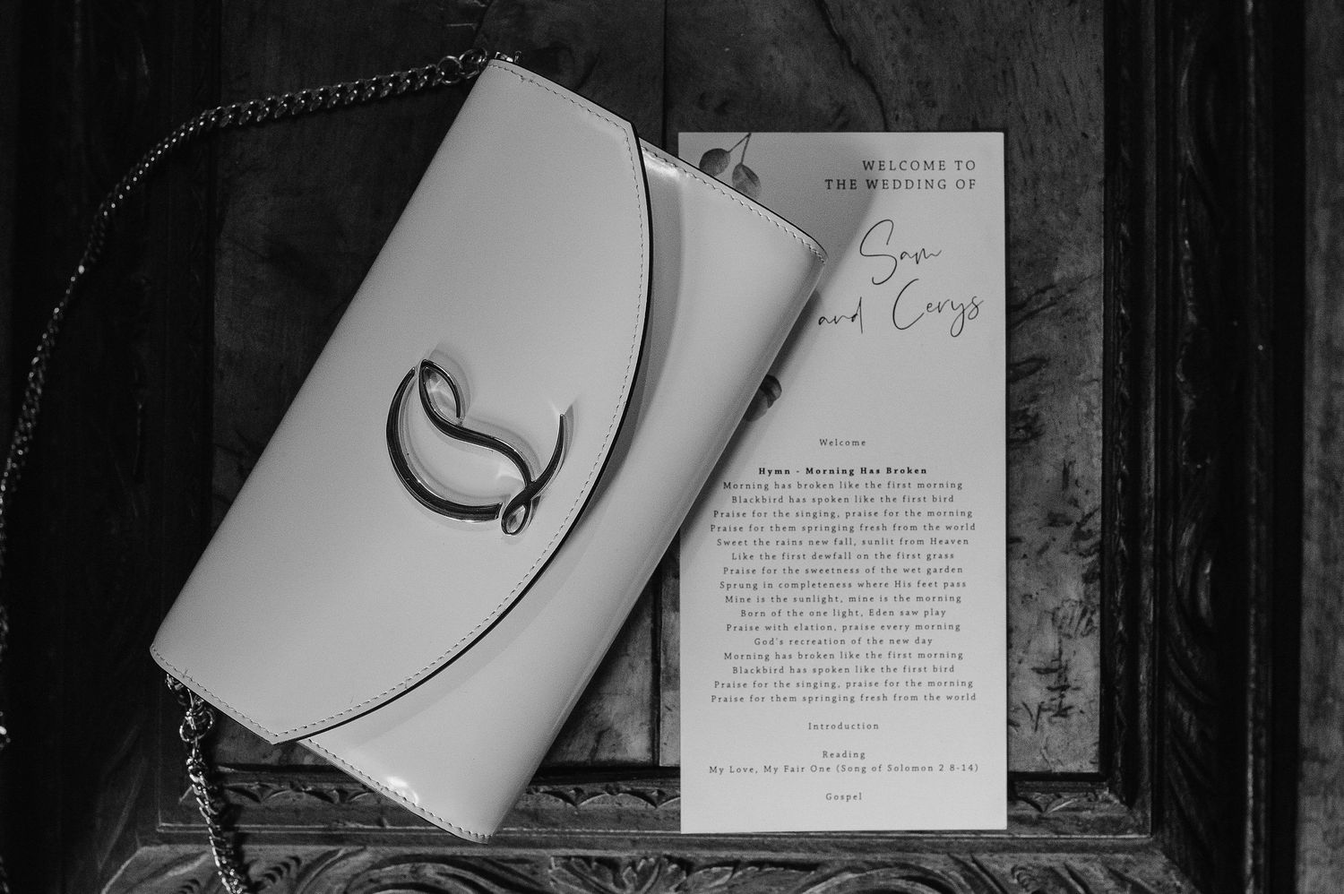Black and white photo of wedding invitation and clutch purse on dark surface.