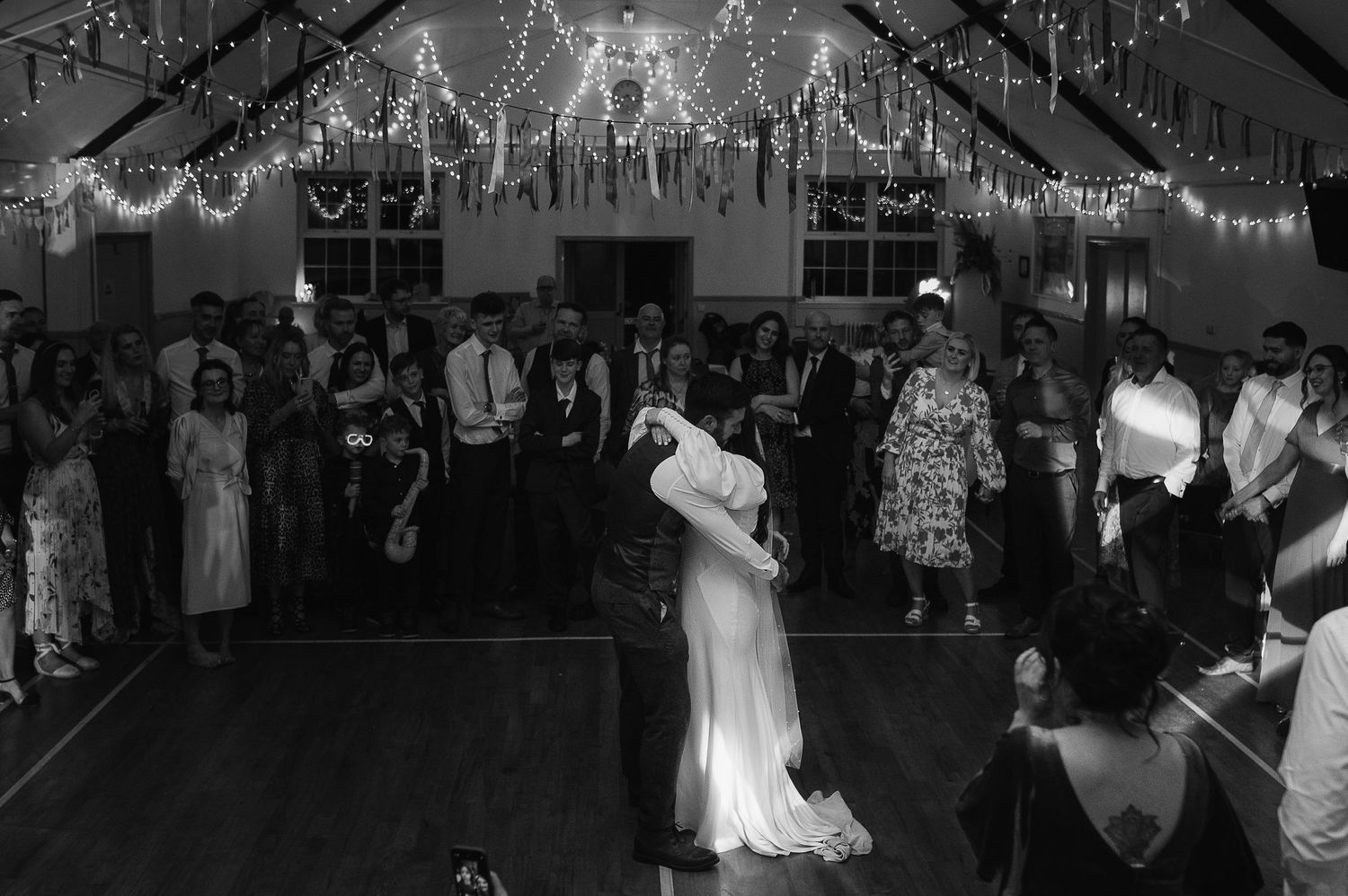 A couple shares their first dance at a wedding reception under twinkling string lights.
