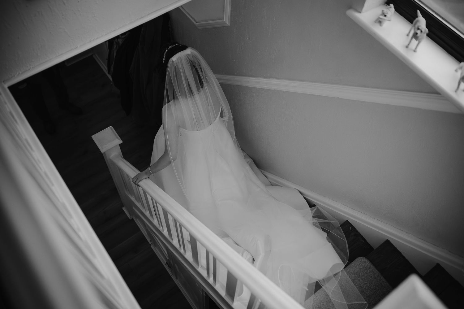A bride in a flowing white dress descending a staircase, captured in black and white.