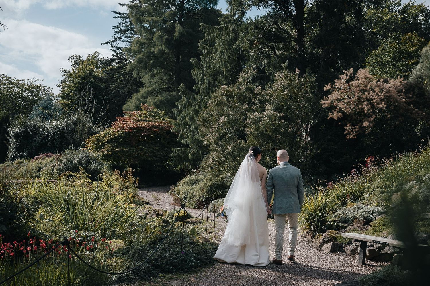 Newlyweds walk hand in hand through a lush garden path on their wedding day.