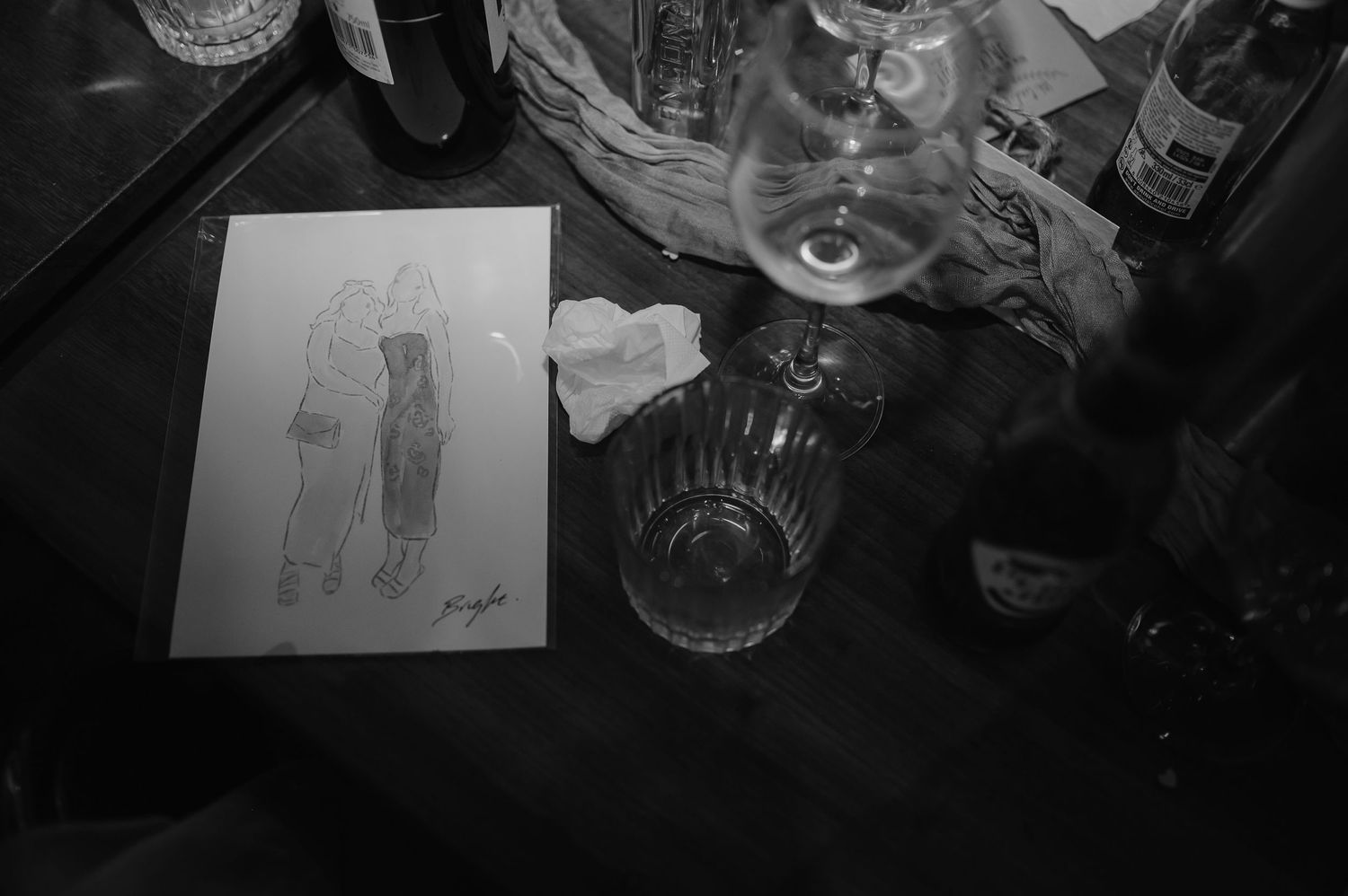 Black and white image of a sketch on paper beside glassware and drinks.