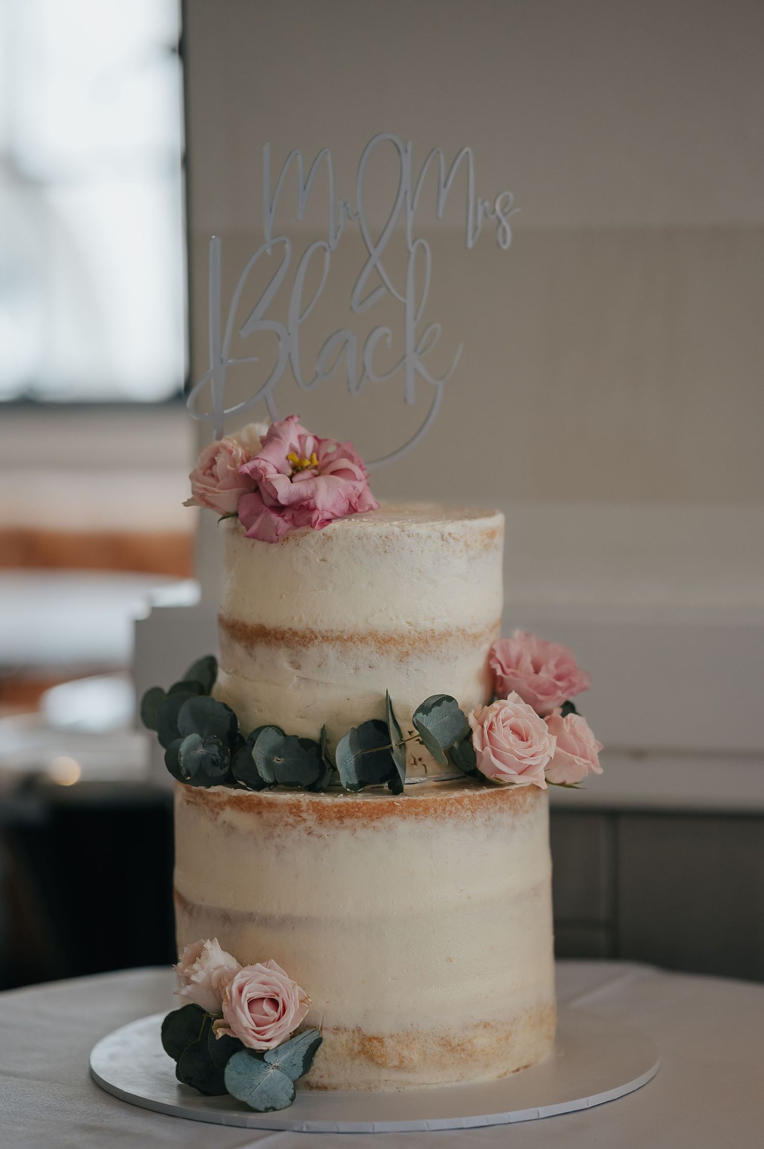 Semi-naked wedding cake decorated with pink roses and eucalyptus leaves.