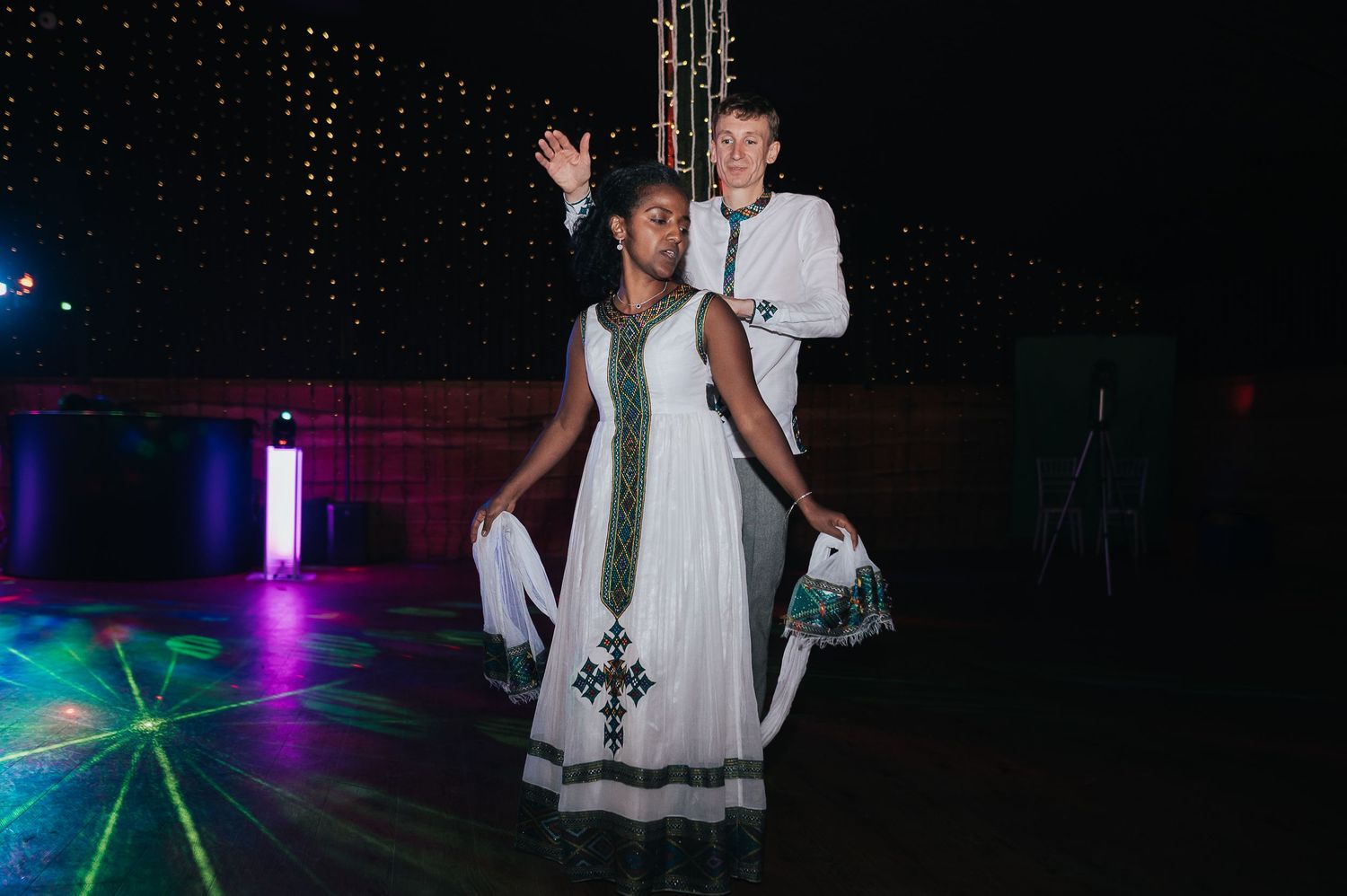 Couple dancing together at a reception with colorful lights and decorative backdrop.