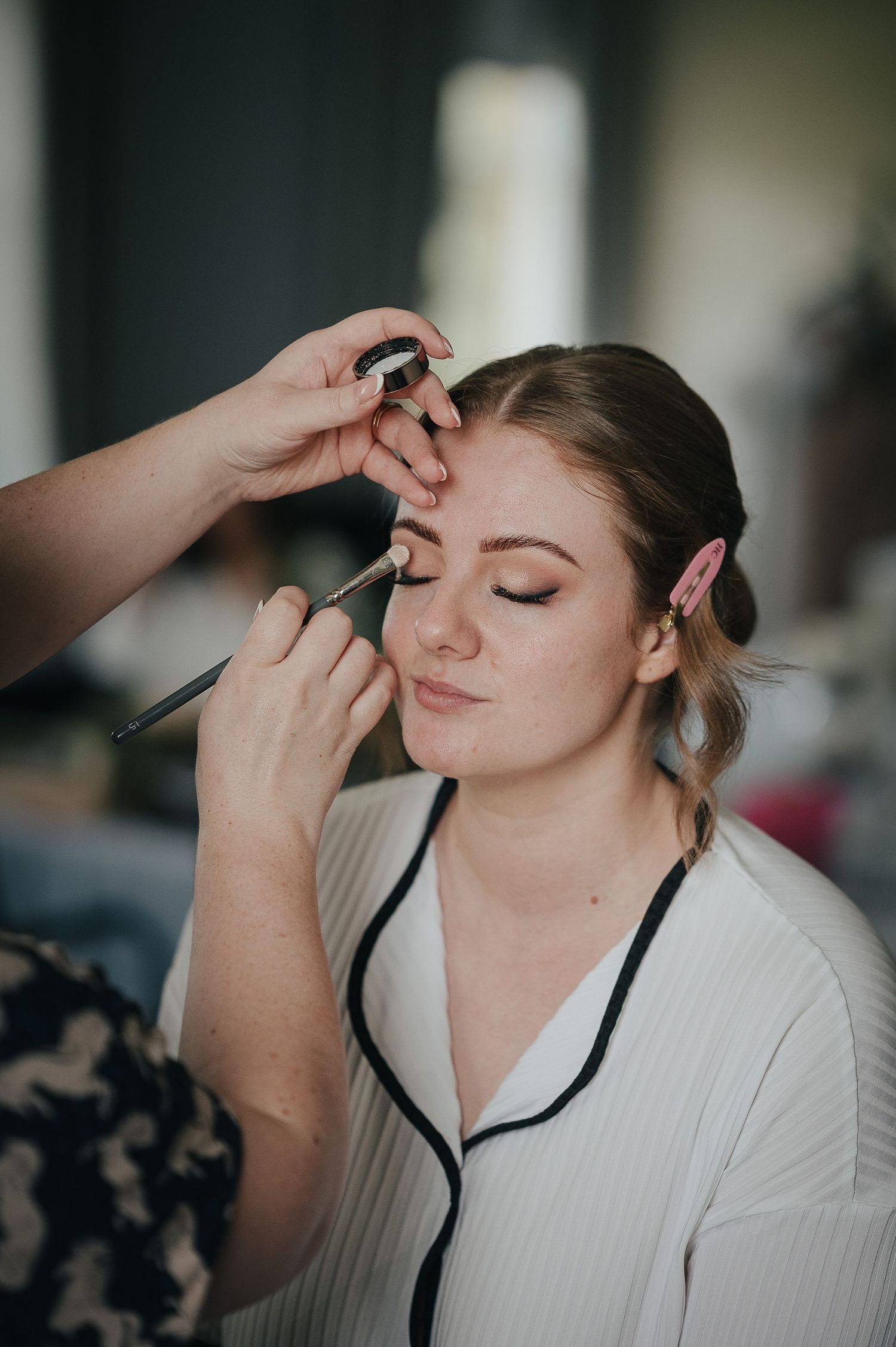 Professional makeup artist applying cosmetics to a relaxed bride during wedding preparations.