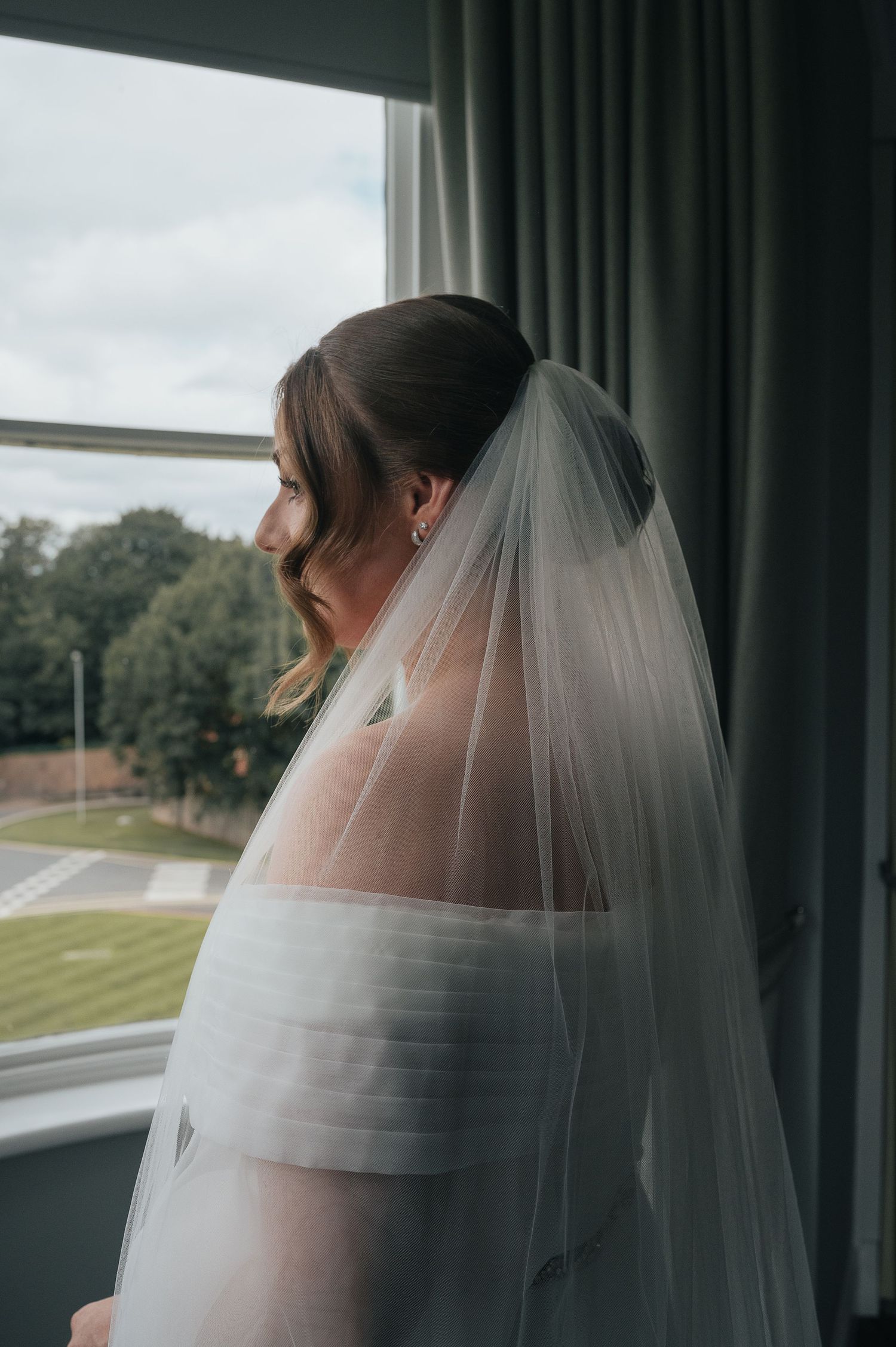 Side view of a wedding dress and veil silhouetted against a window.