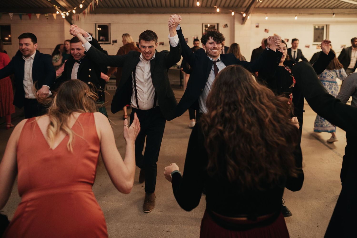 Wedding guests dancing and celebrating at an indoor reception with ambient lighting.