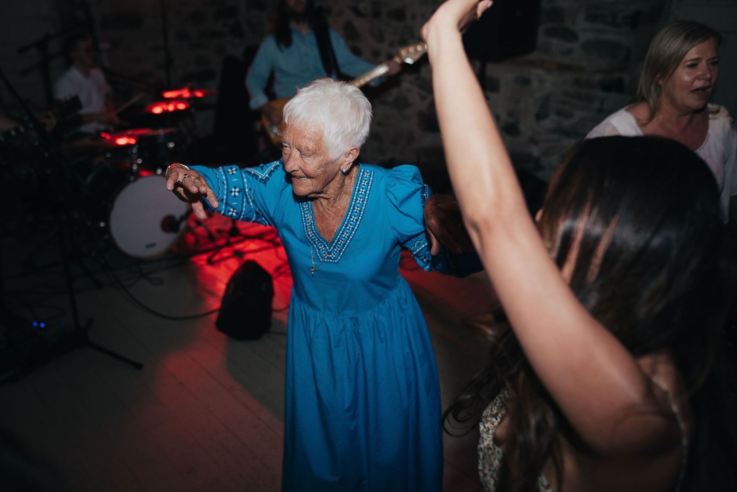 Woman in blue dress joyfully dancing at a wedding reception under red lights.