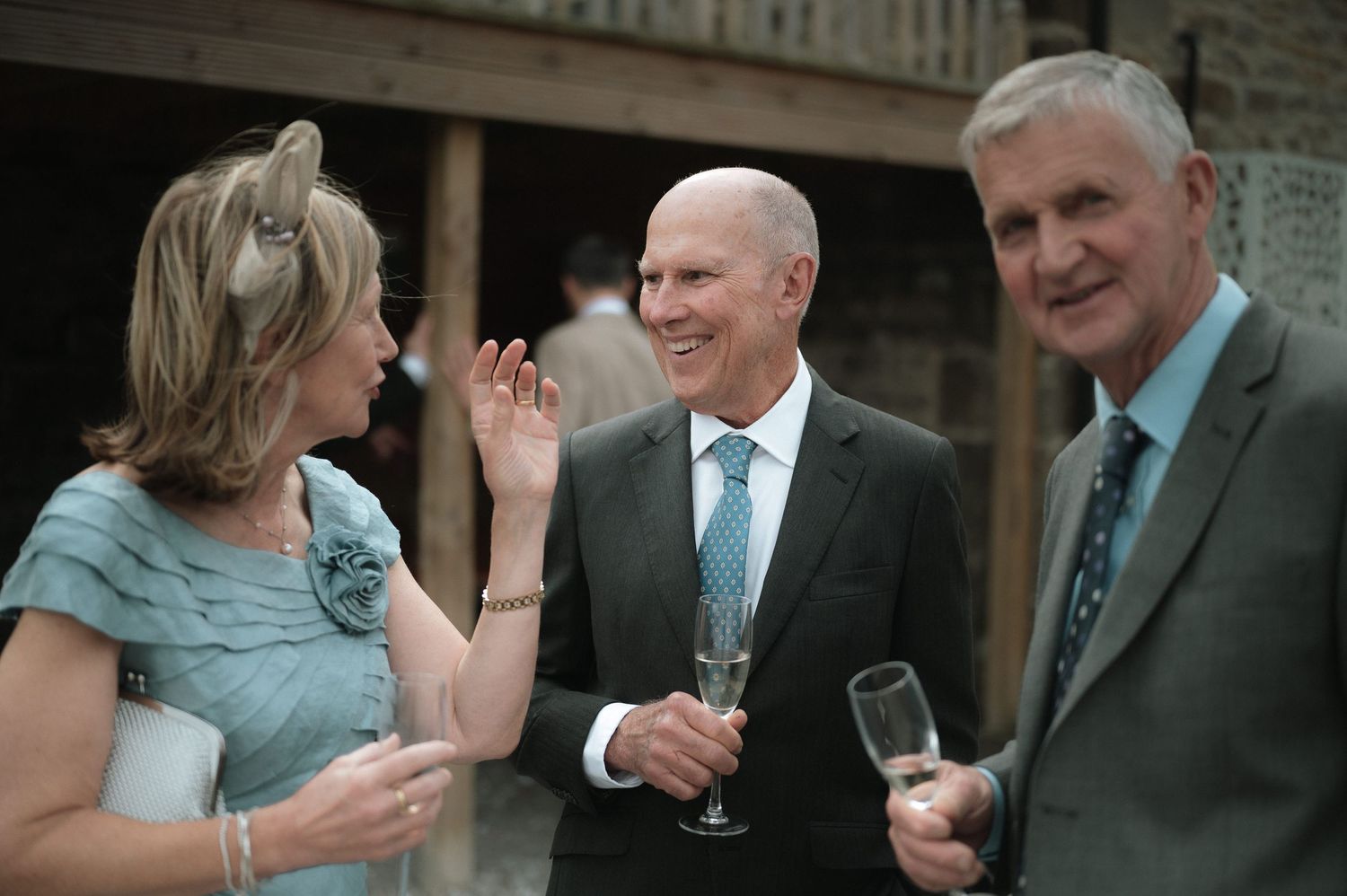Three elegantly dressed guests enjoying conversation and drinks at an outdoor event.