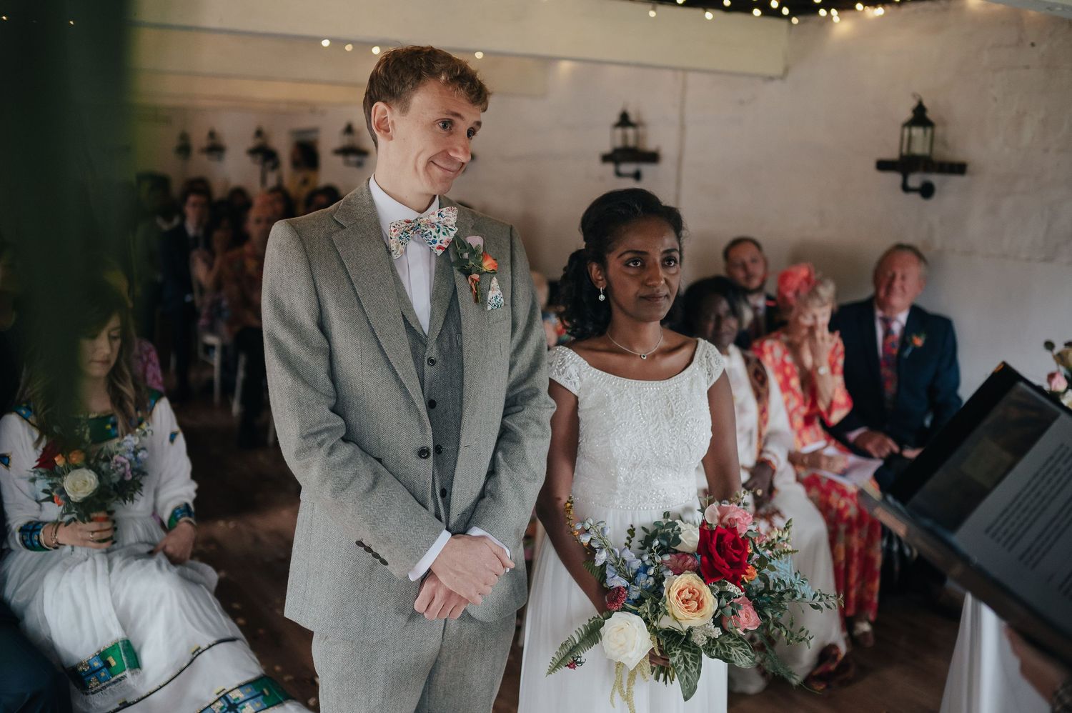 A wedding ceremony in progress with guests seated in a light-filled room with lantern decorations.