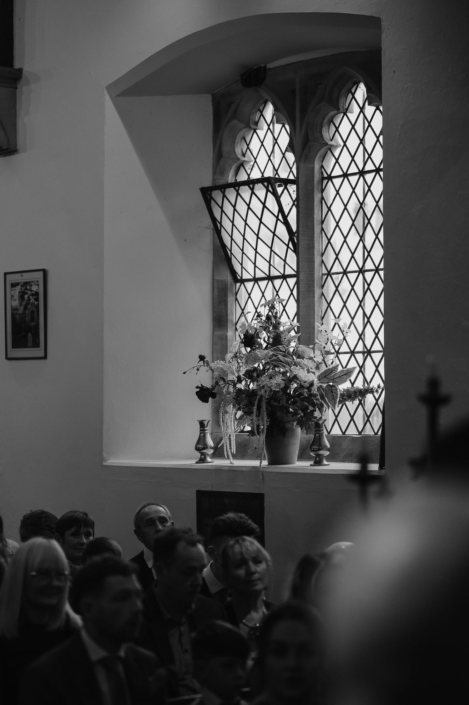 Black and white photo of a church window with floral arrangement and gathered congregation below.
