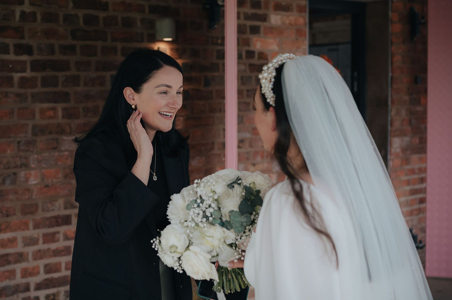An intimate moment between wedding guests with white bouquet against brick wall backdrop.