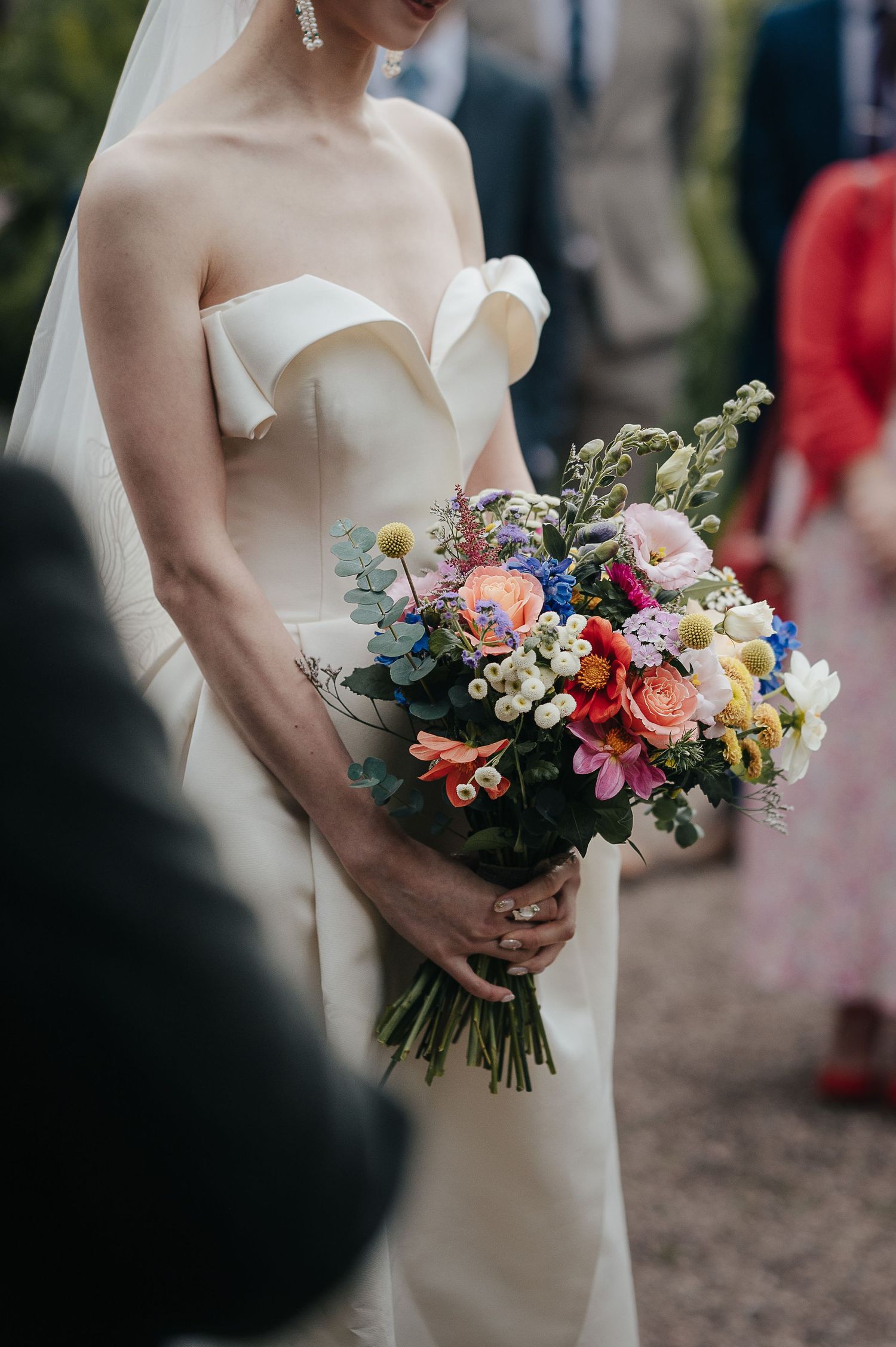 Close-up of a colorful bridal bouquet with mixed flowers held against a white wedding dress.