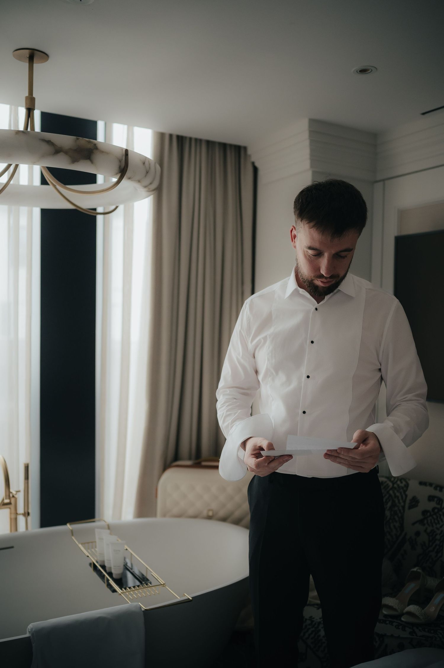 A person in a crisp white shirt reads a document while standing in a modern, well-lit room with elegant decor.