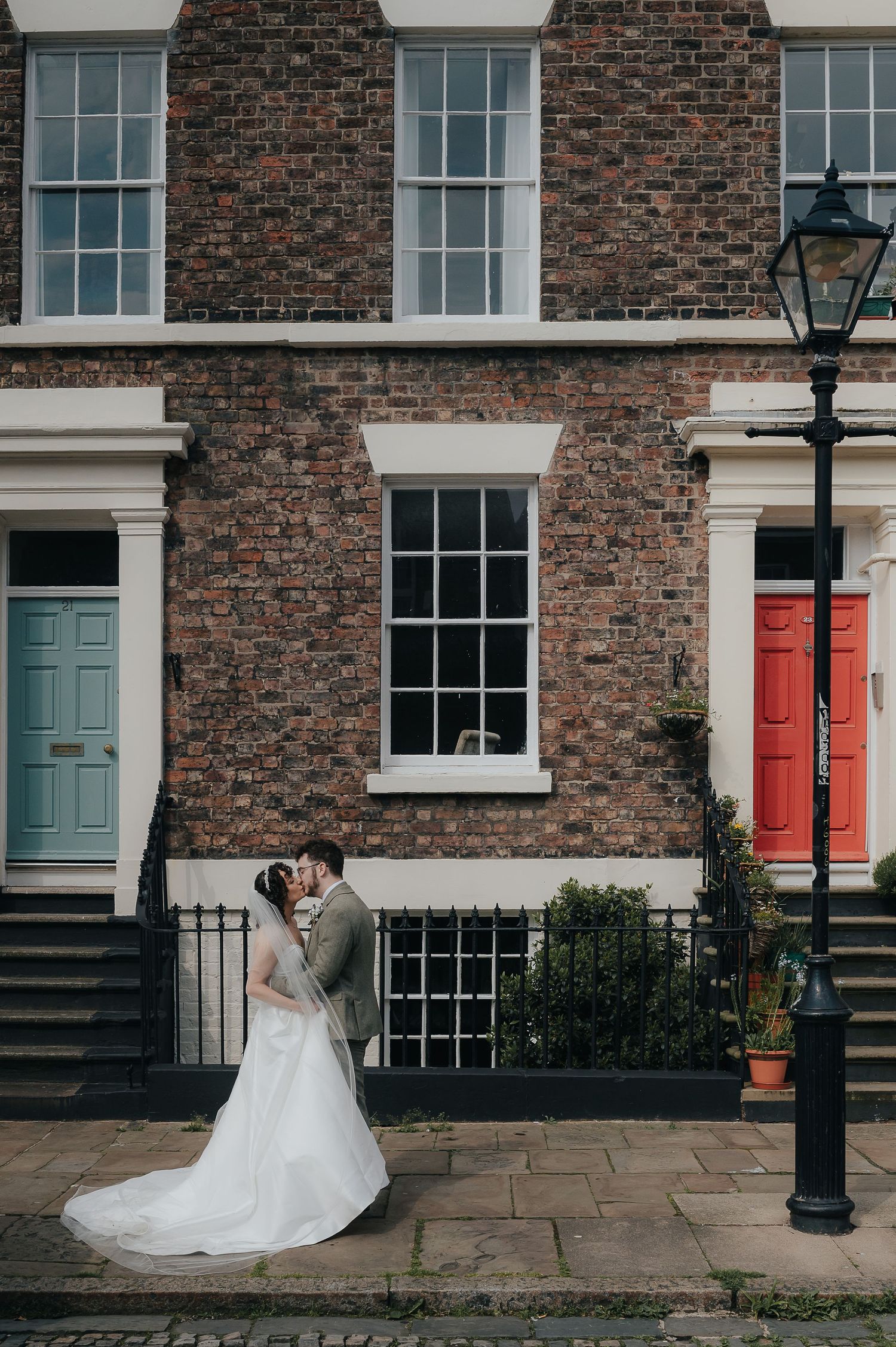 A romantic moment captured against a historic brick building with contrasting blue and red doors.
