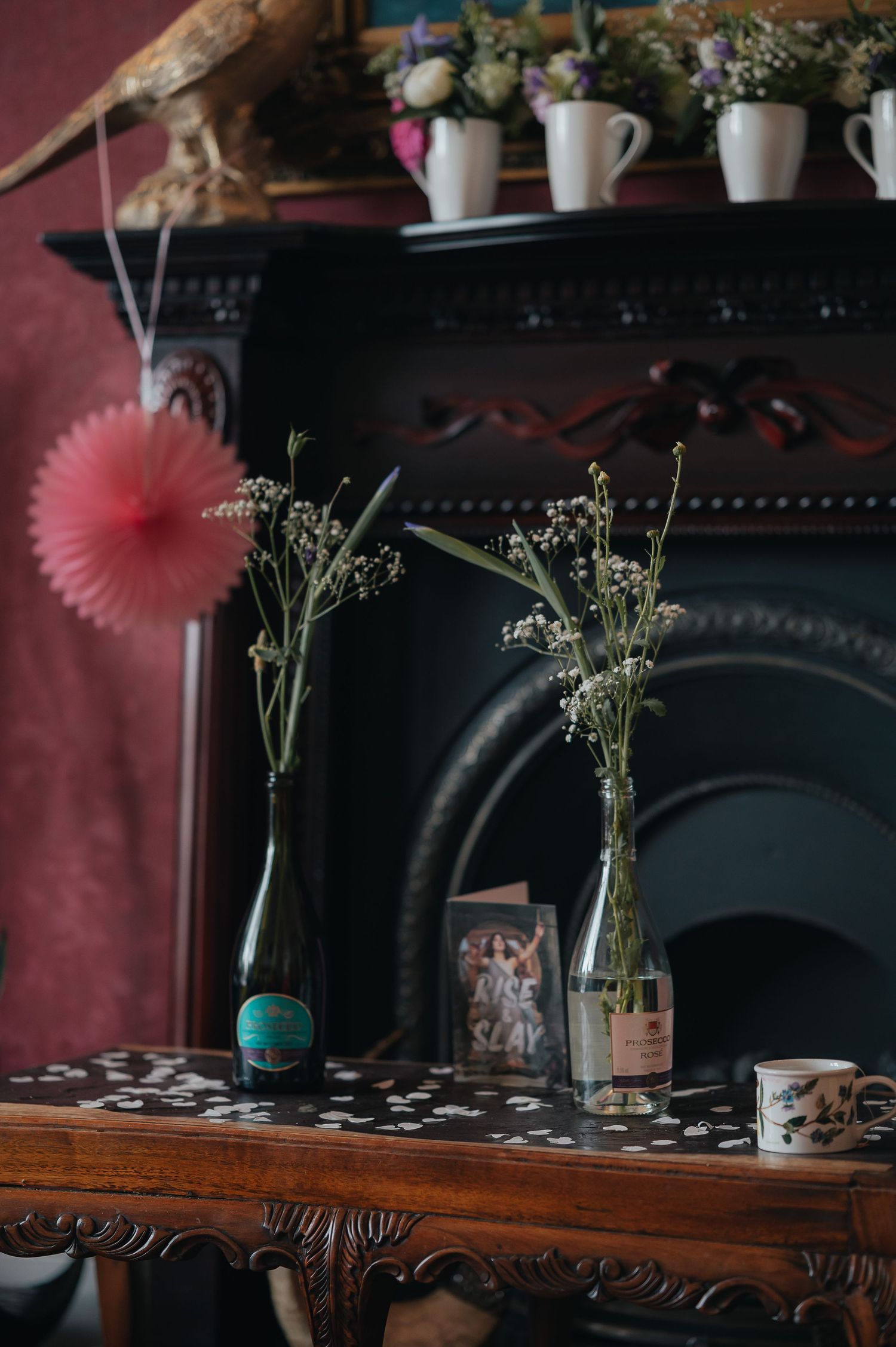 Simple floral arrangements in glass bottles displayed on wooden mantle against burgundy wall.