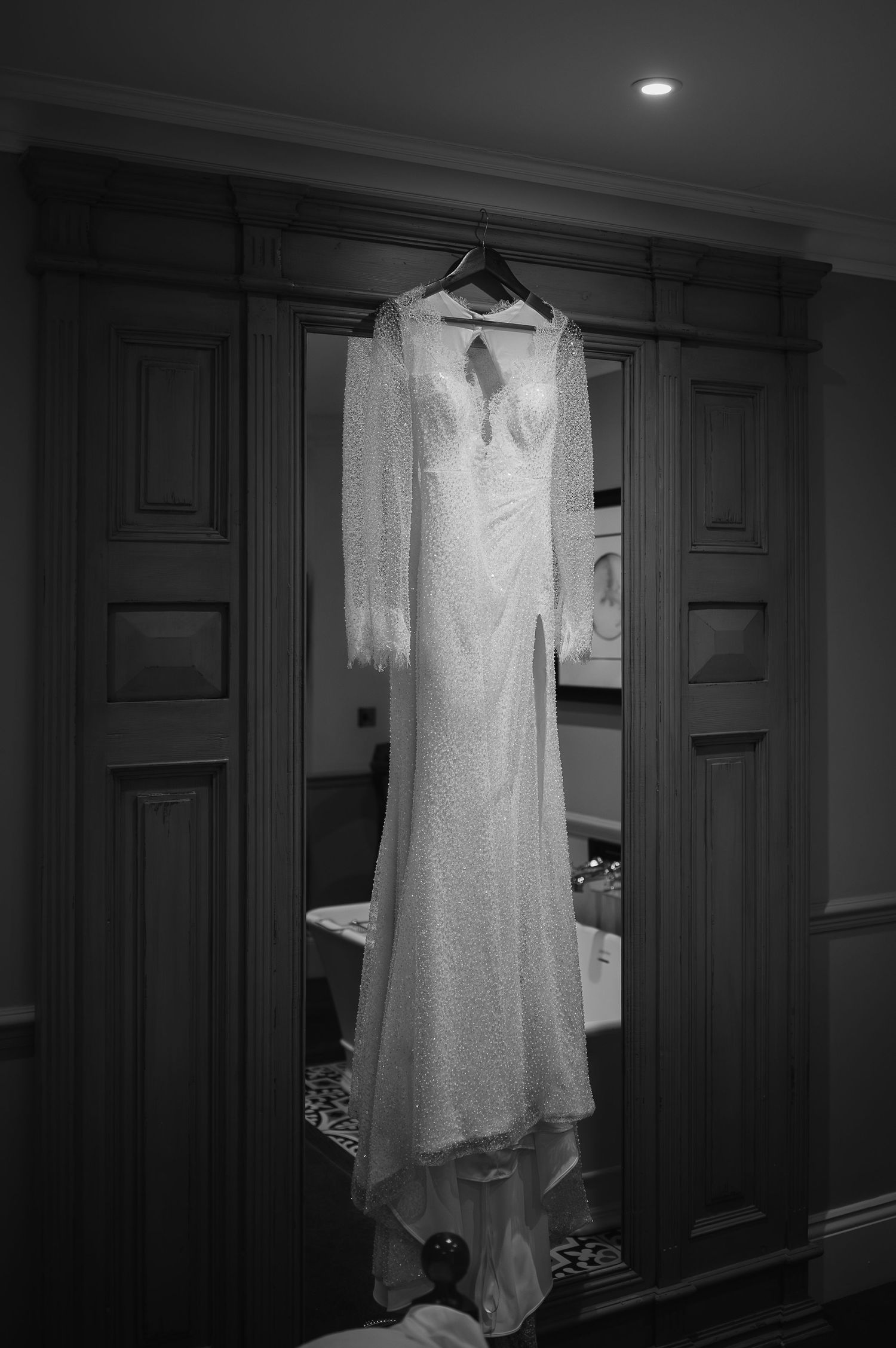 Elegant white wedding dress with lace details hanging against dark wooden panels.